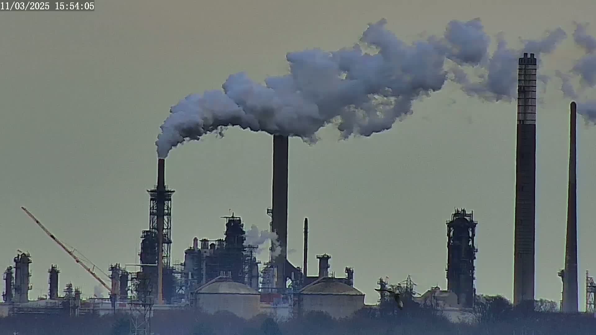 A large industrial complex with several tall smokestacks emitting plumes of smoke into an overcast sky.