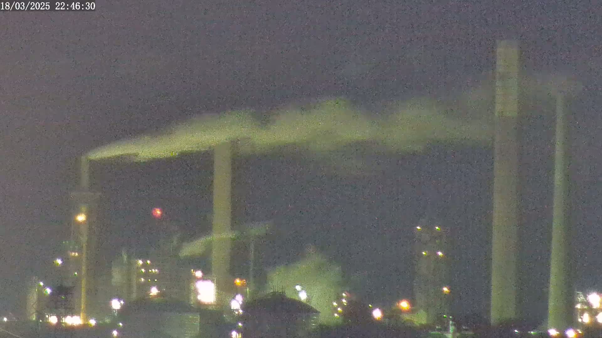 At night, an industrial plant with tall smokestacks releases plumes of smoke into a dark sky.