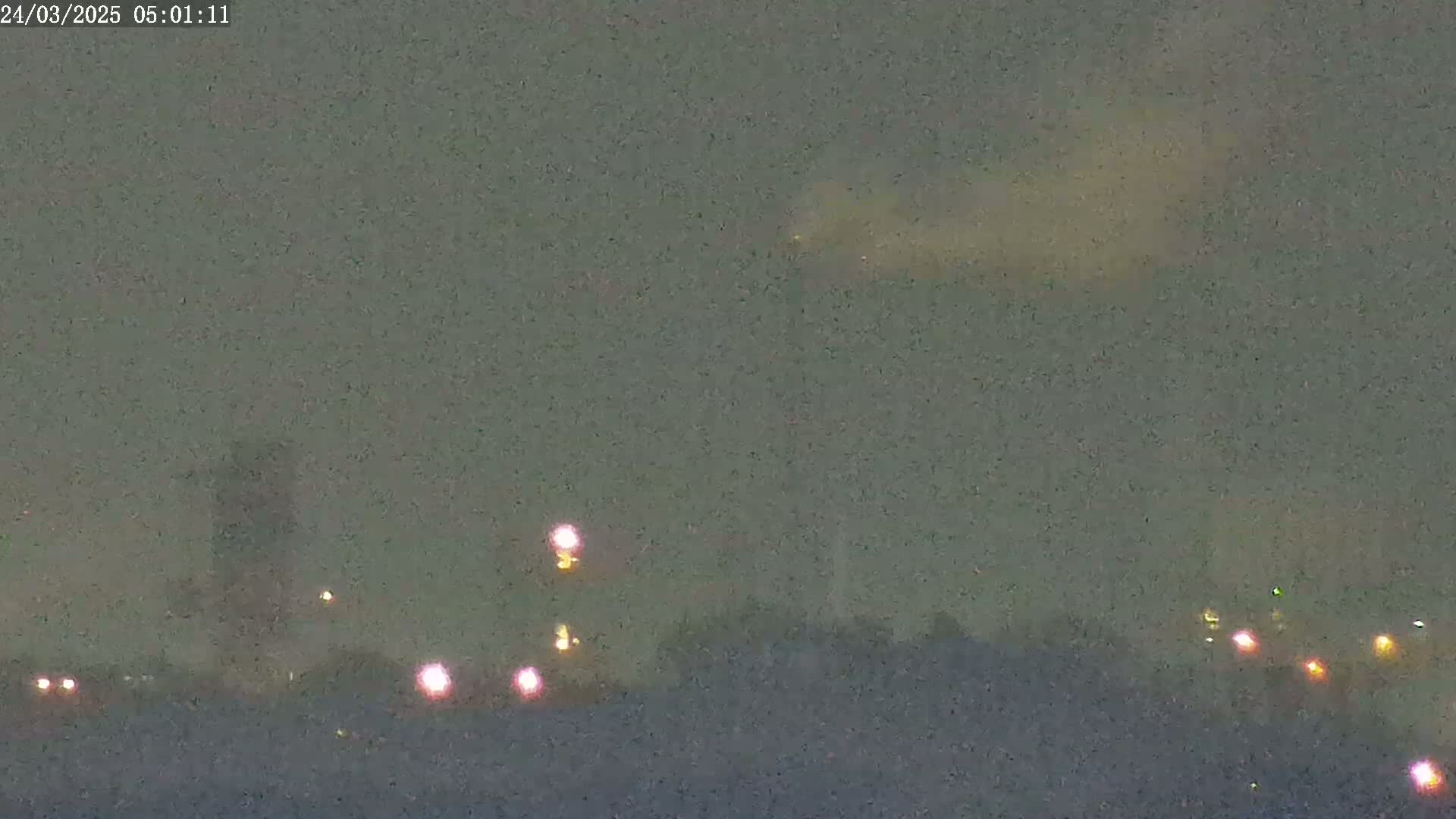 A hazy, dark sky shows a distant, faint light source above a line of dim lights on the horizon.
