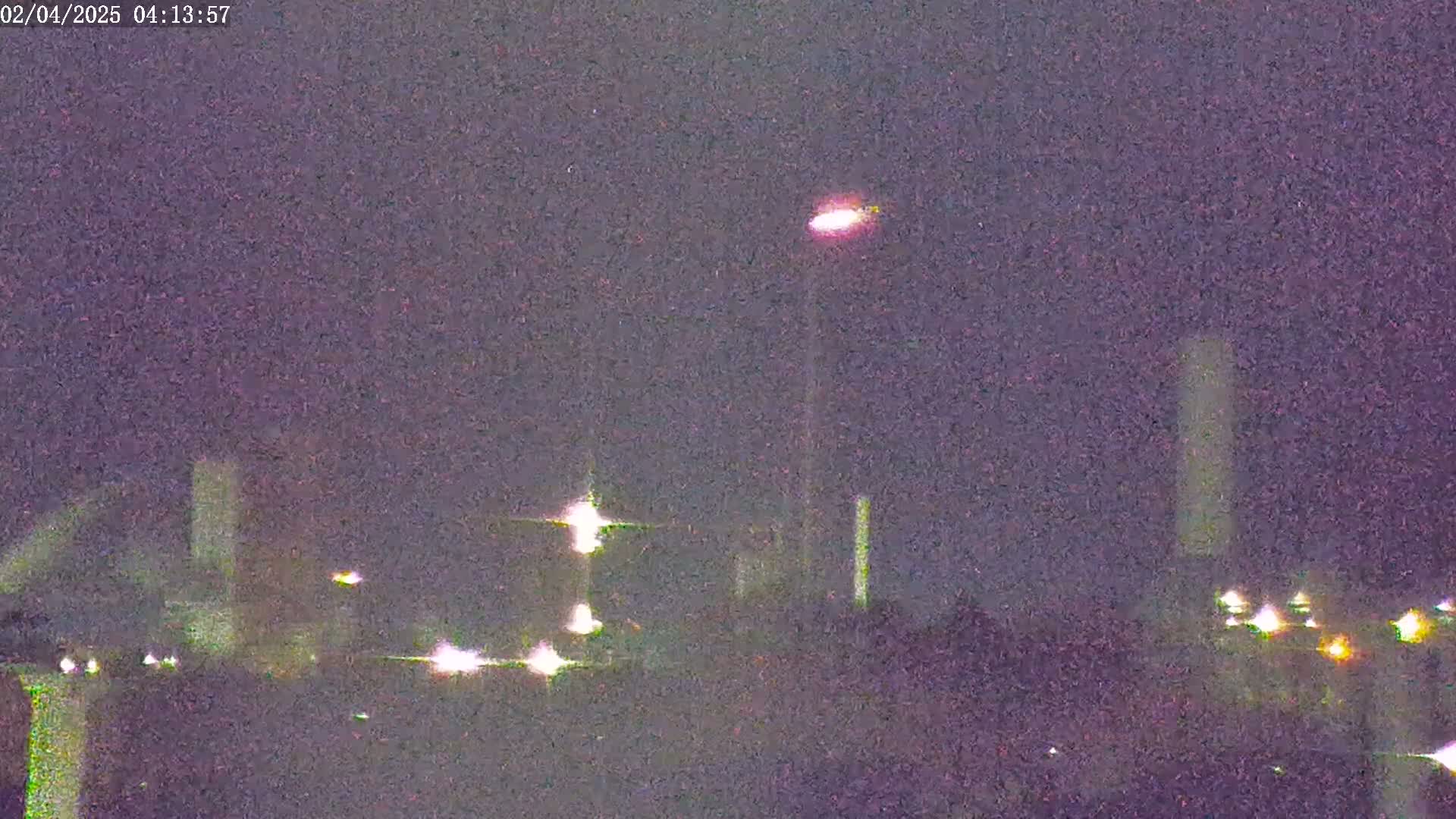 A nighttime long shot shows an industrial area with lights and tall structures under a dark, possibly cloudy sky.