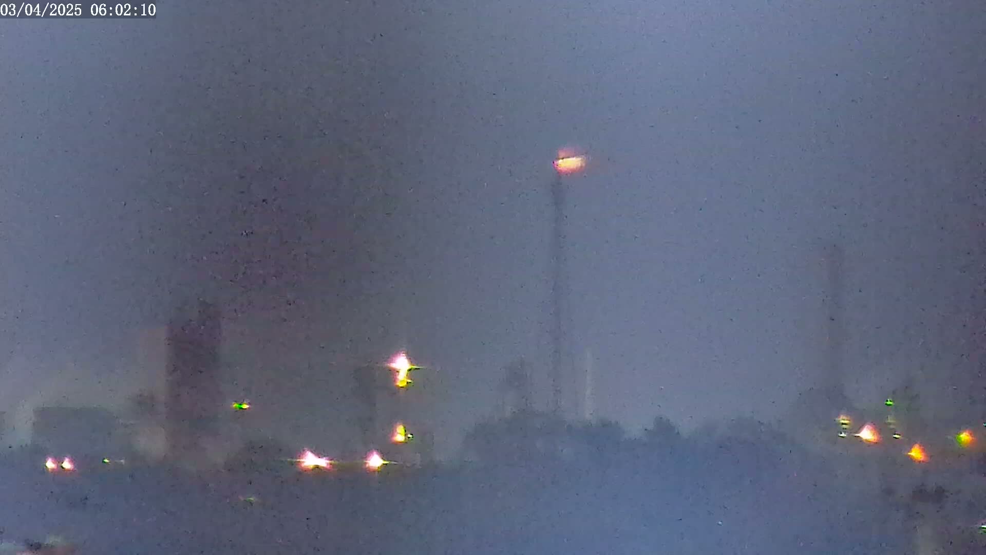 Several tall structures with bright lights are visible through a hazy, dark atmosphere.