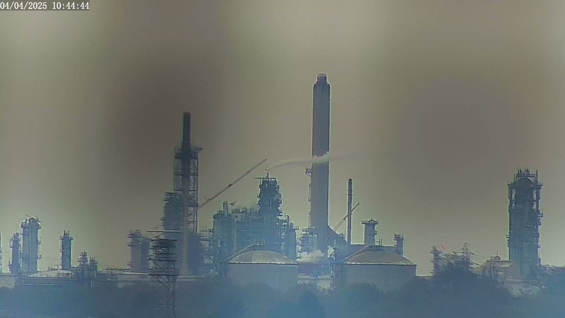 A hazy view of an industrial plant with several tall smokestacks emitting a small amount of smoke.