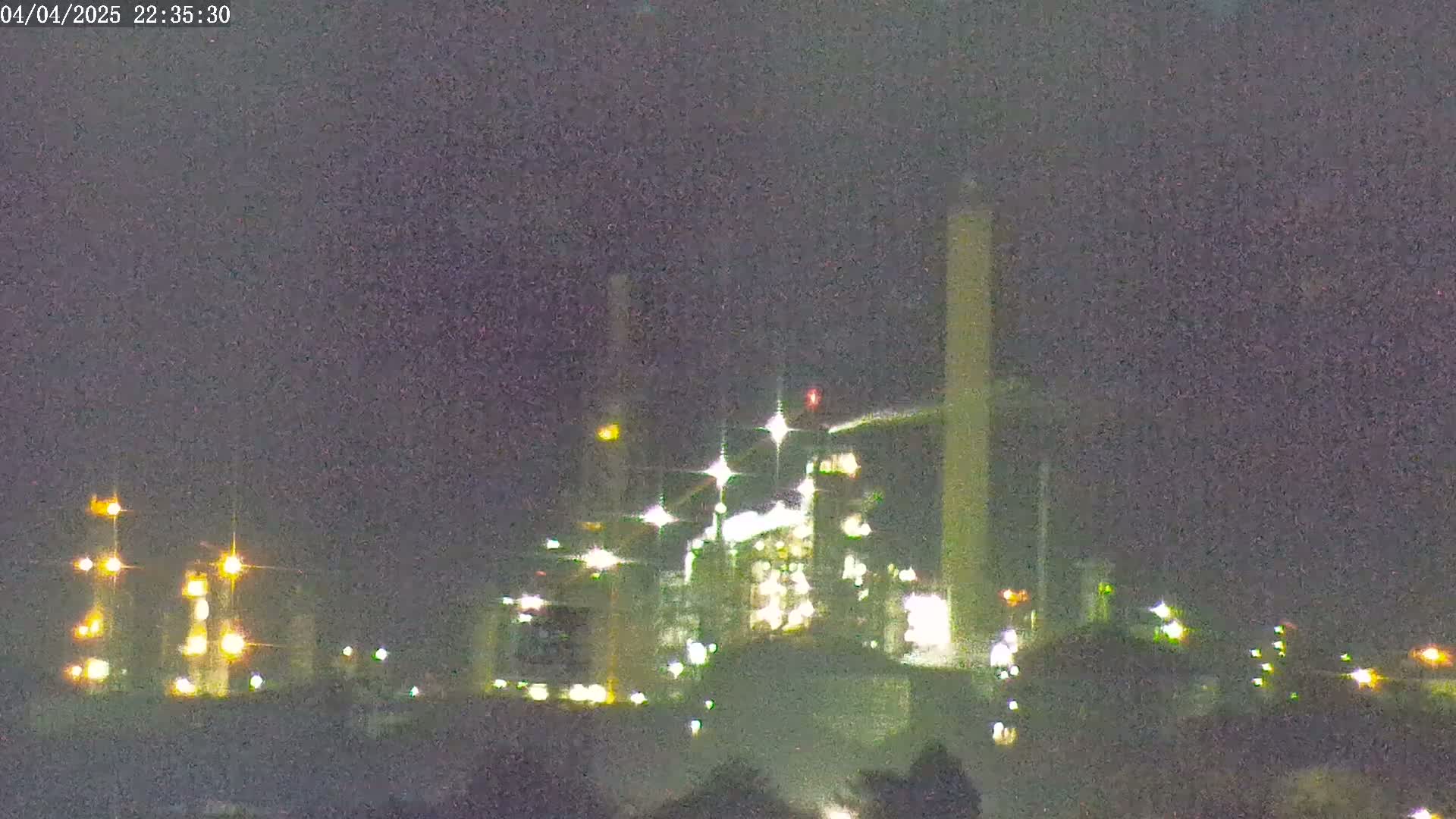 At night, under a dark sky, an industrial complex with numerous lights illuminates the landscape.
