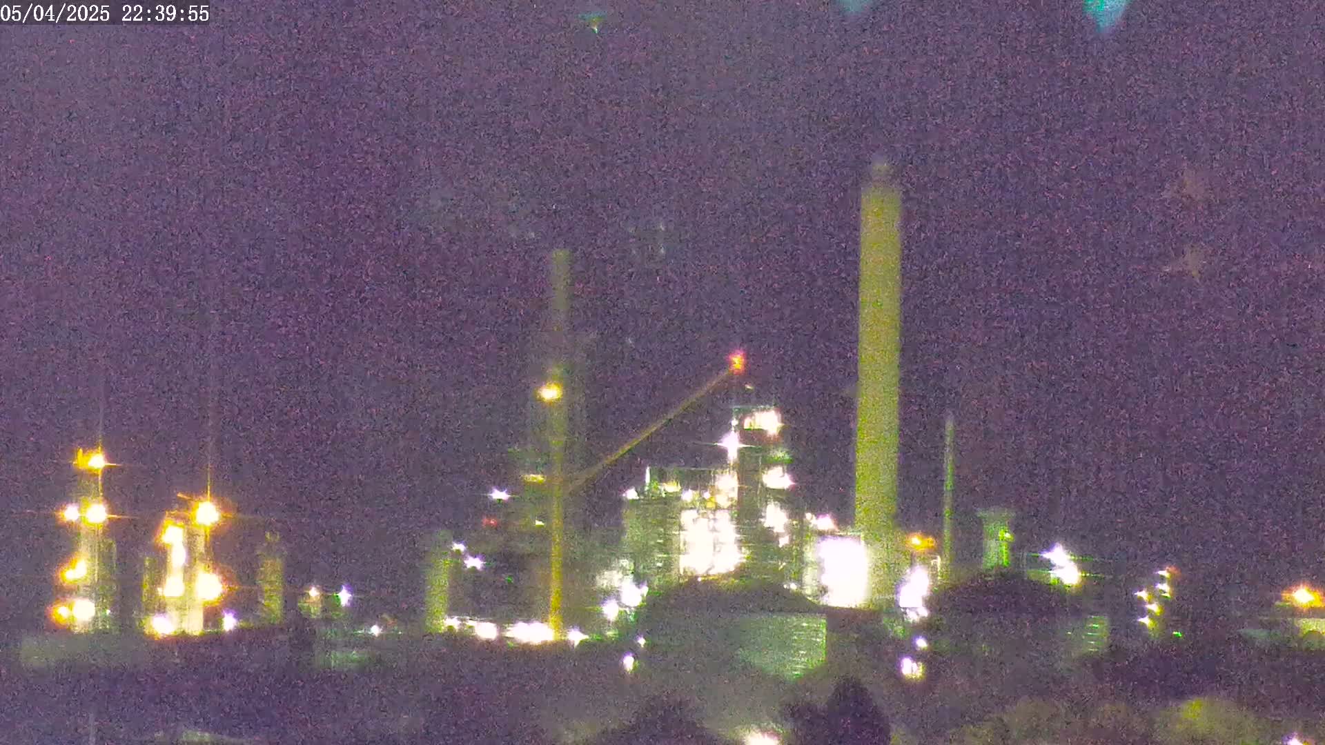 A brightly lit industrial plant is visible at night under a dark, mostly clear sky.