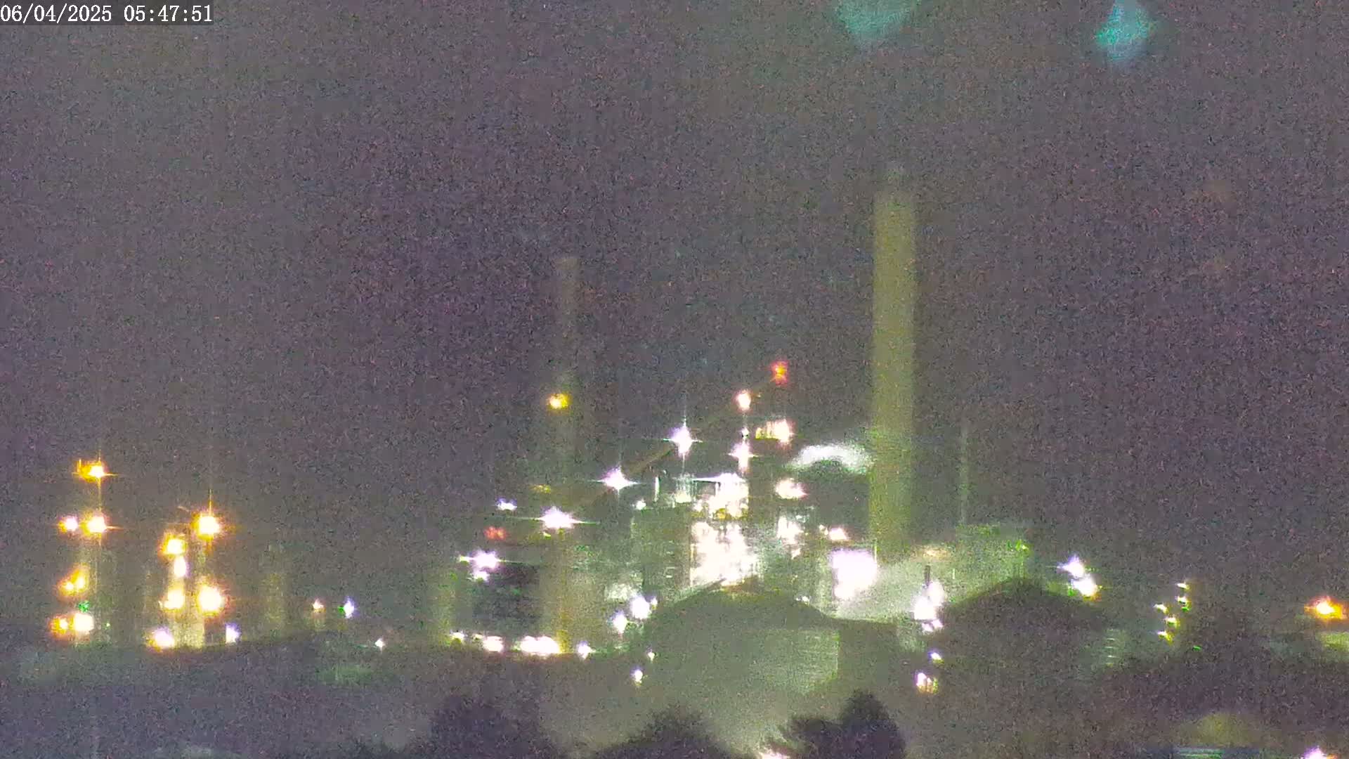 A brightly lit industrial complex is visible at night under a hazy sky.