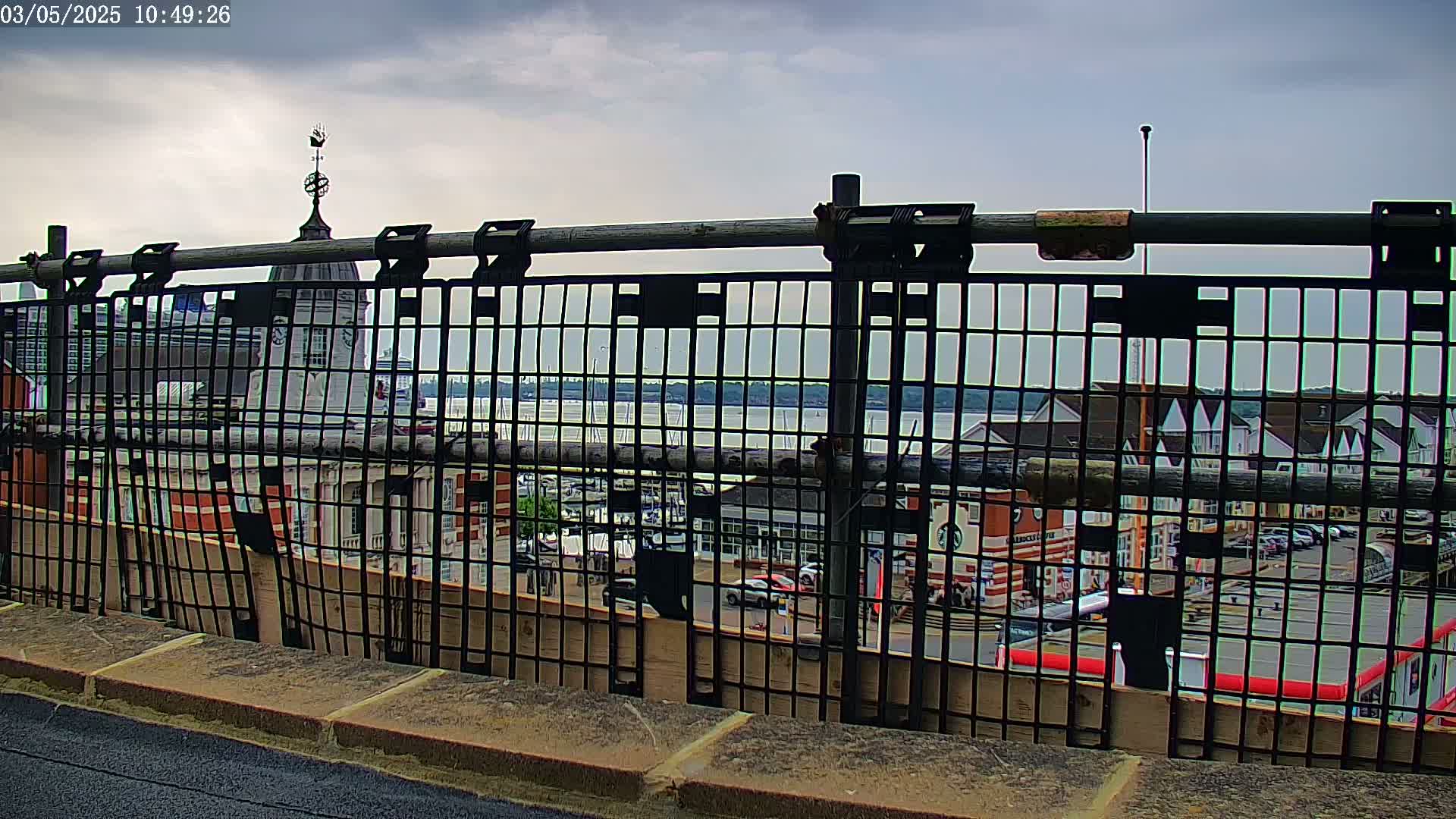 A view of a harbor and town is seen through a metal fence on an overcast day.