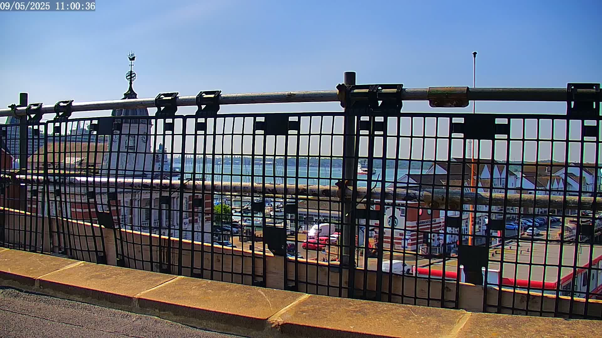 A metal fence with a view of a harbor, buildings, and a clear blue sky.