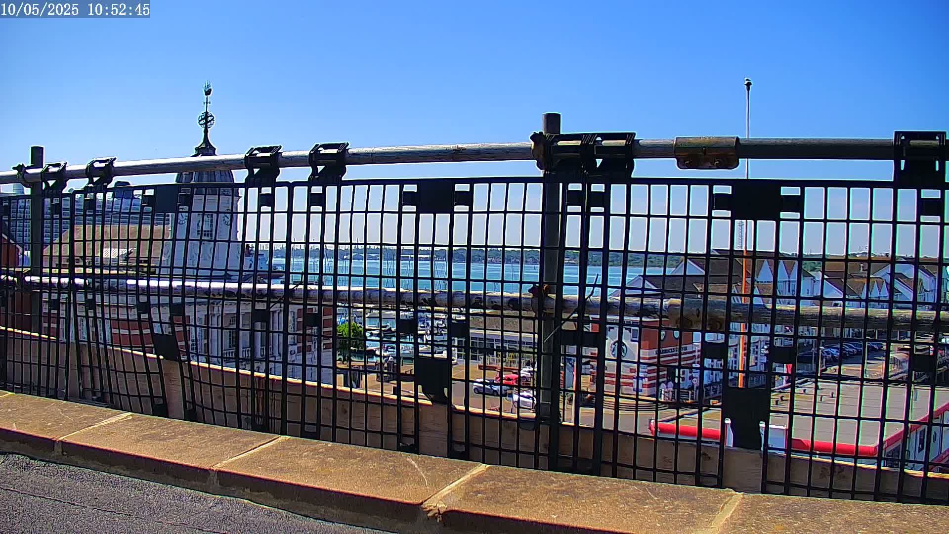 A metal railing overlooks a harbor filled with boats on a sunny day.