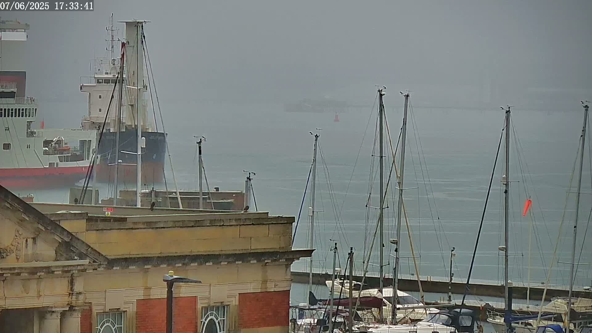 A cargo ship and several sailboats are moored in a harbor on a foggy day.