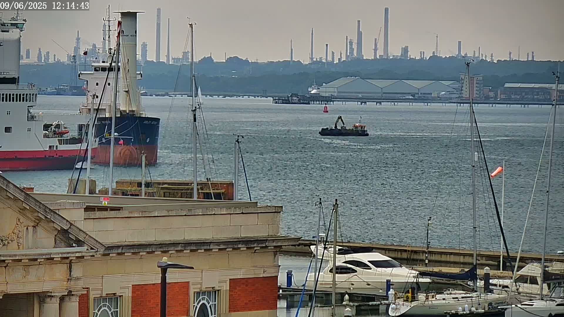 Several ships are on a body of water with a hazy sky in the background, featuring an industrial skyline and docked sailboats in the foreground.
