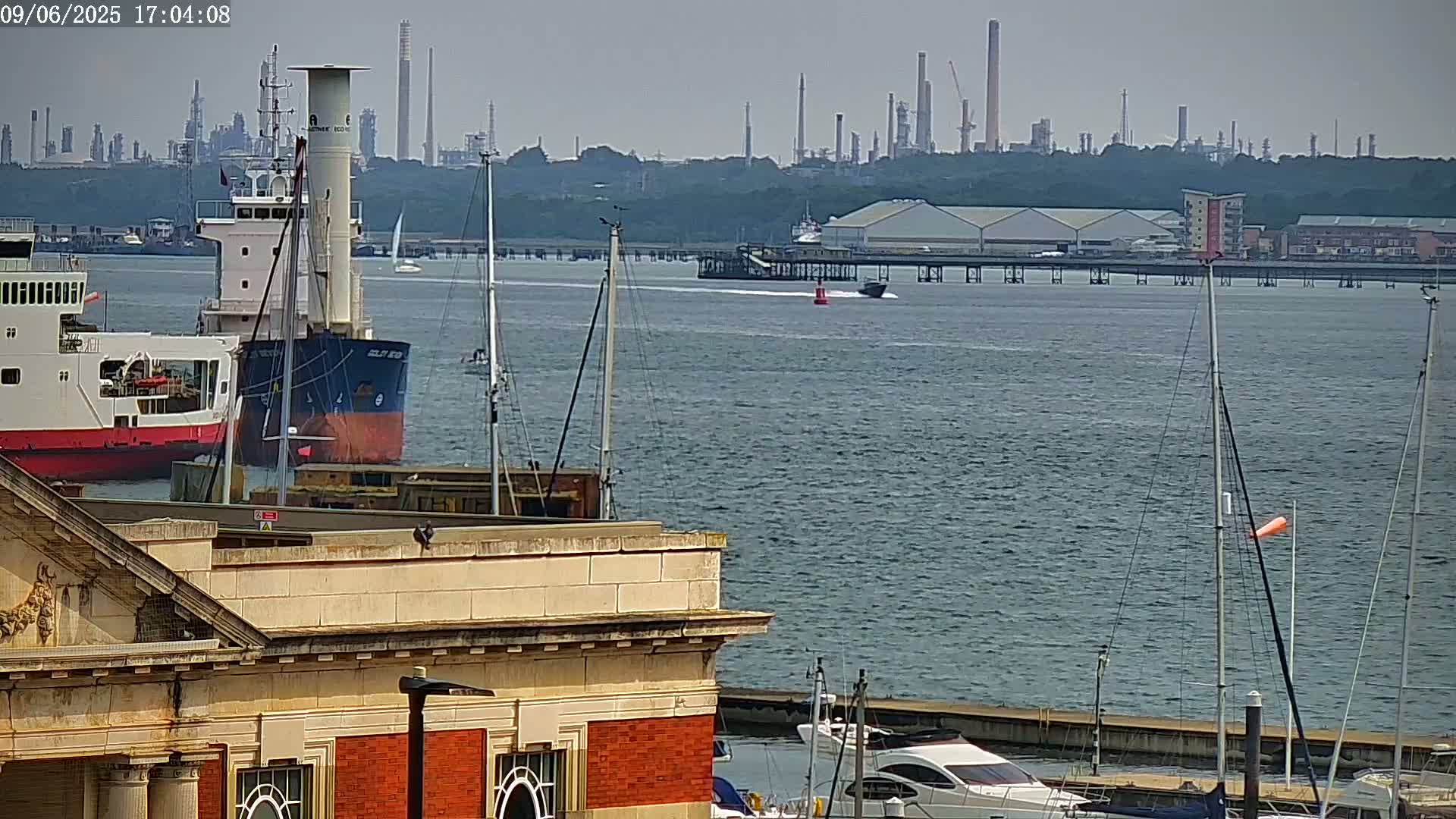 A view from a building overlooking a calm body of water with several ships and boats, including a large cargo vessel, and an industrial area in the background.