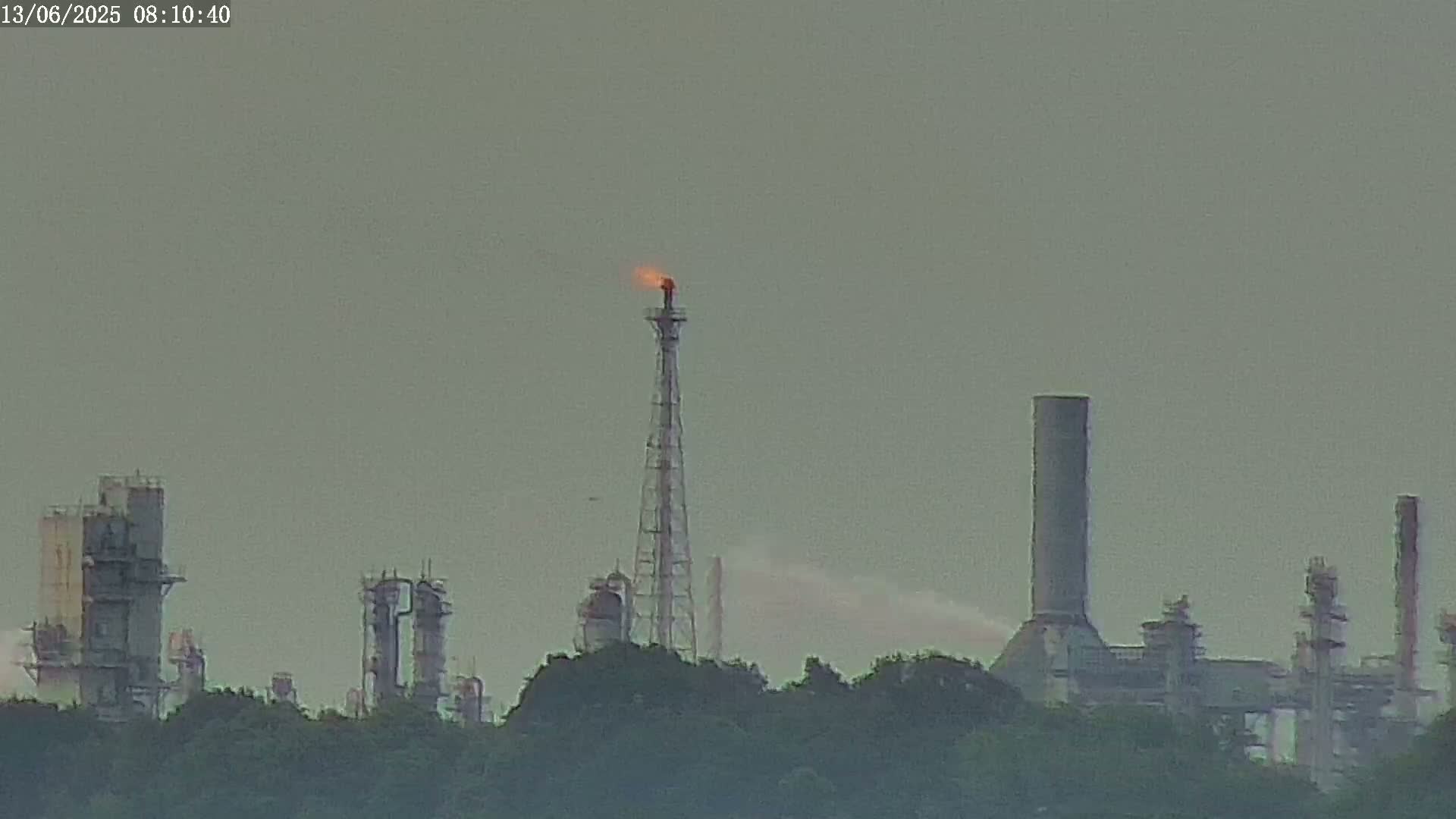 An industrial plant with tall structures and a burning flare stack is visible under an overcast sky.