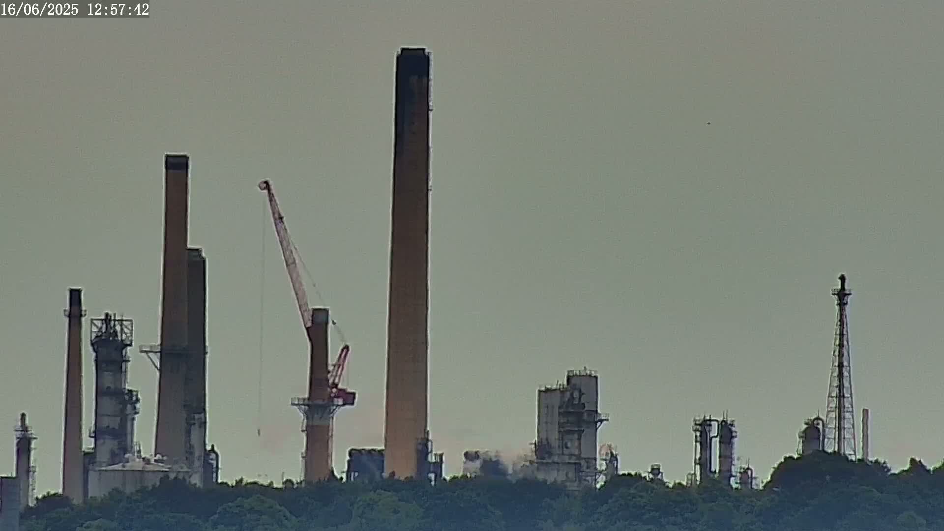 A large industrial complex with numerous tall smokestacks and a crane is visible on a hazy day.