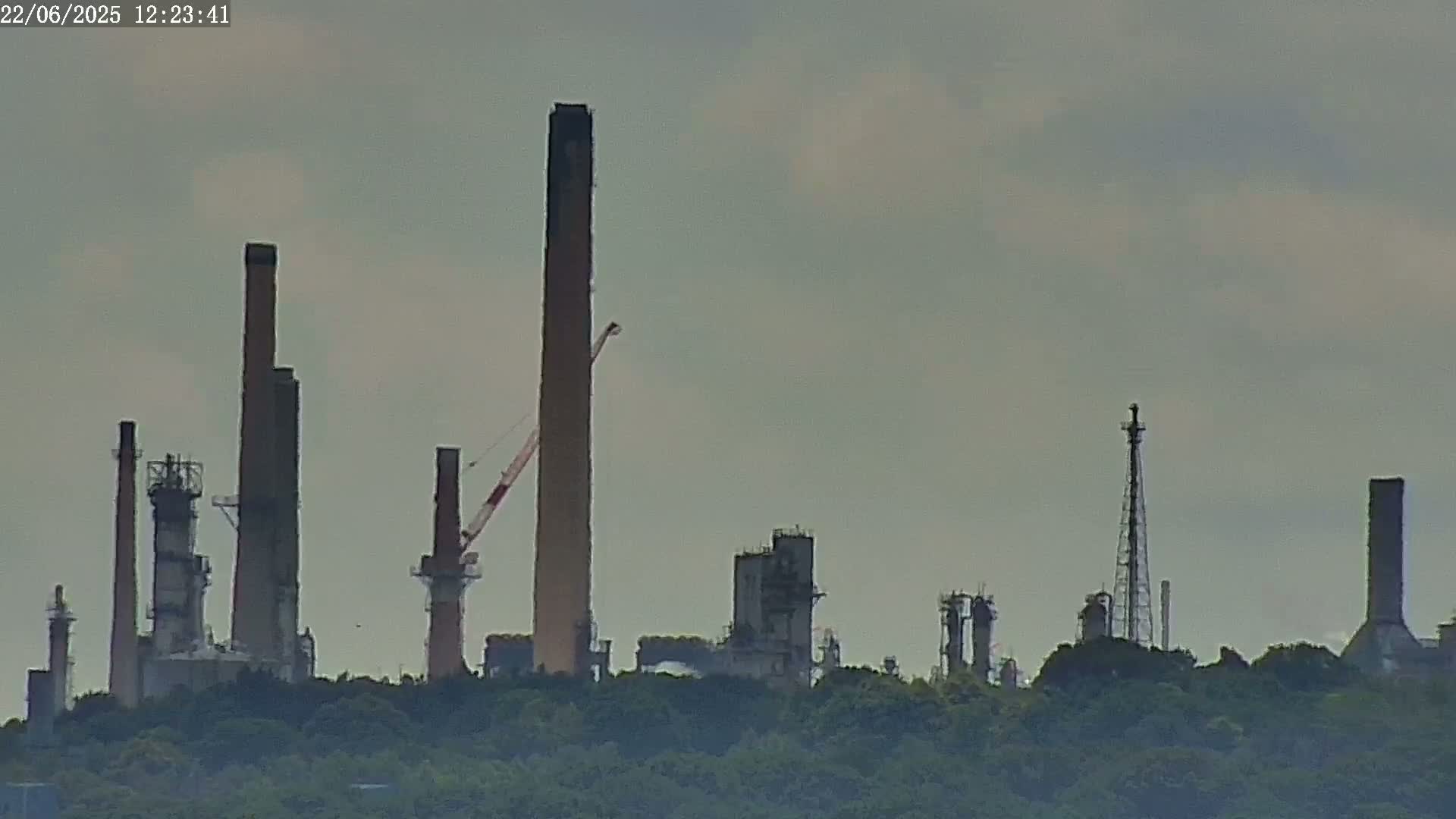 An industrial plant with numerous tall smokestacks and other structures is seen from a distance on a hazy day.