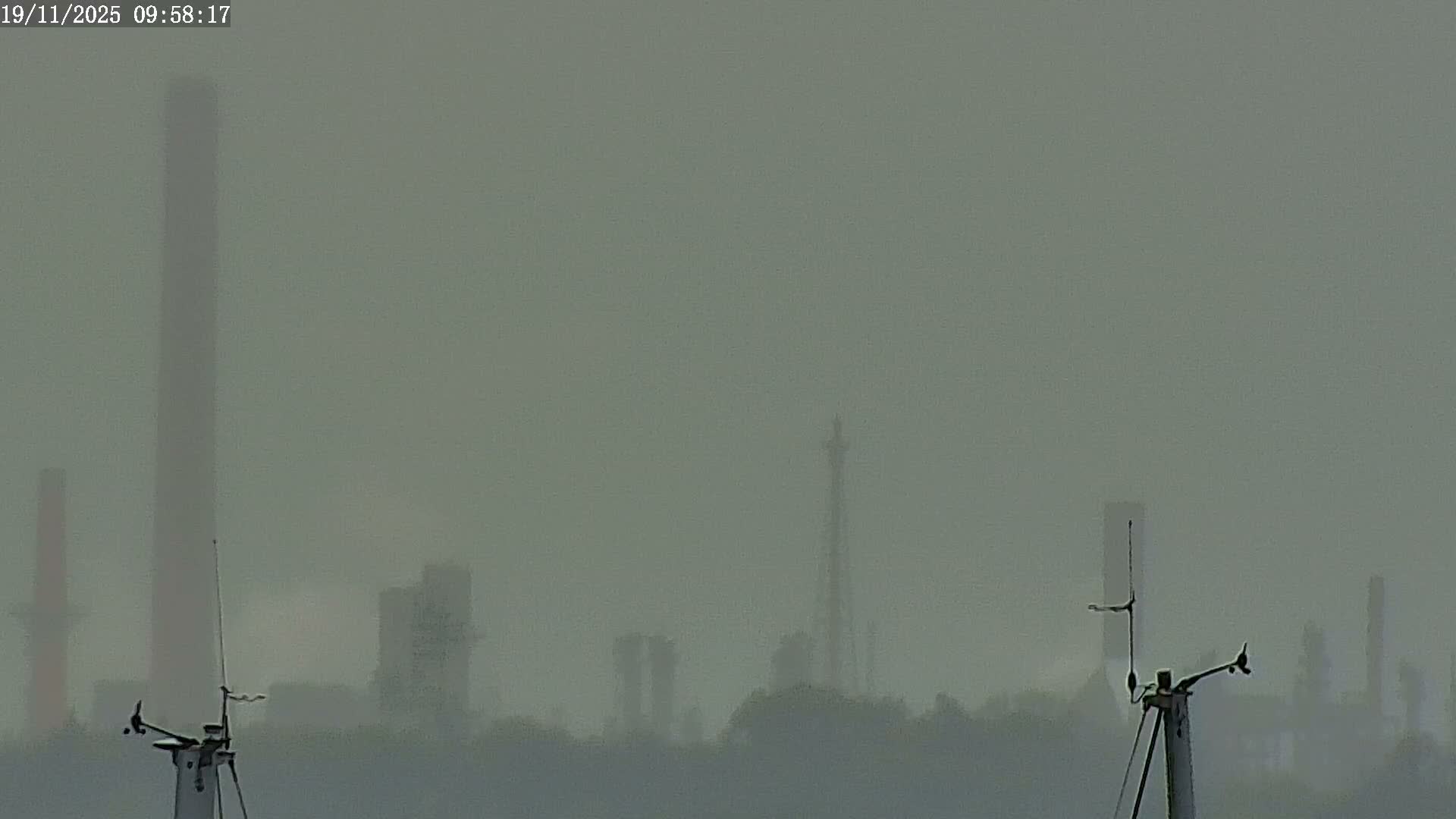 A foggy industrial landscape is visible, featuring tall chimneys and structures partially obscured by the thick atmosphere, with weather monitoring equipment in the foreground.