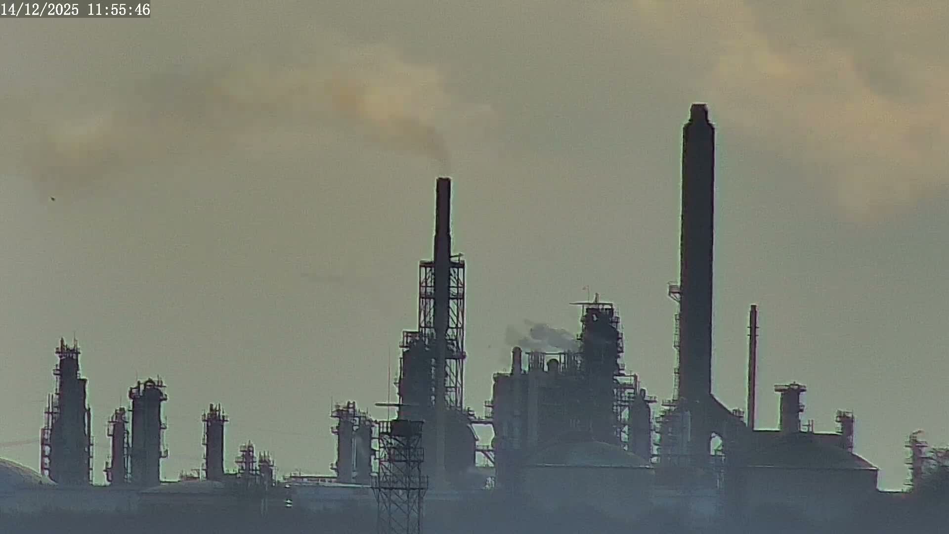 A clear dawn or dusk sky hangs over an industrial scene featuring the top of a blue boat, a flare stack with a bright flame, extensive scaffolding, and numerous factory chimneys emitting plumes of steam.