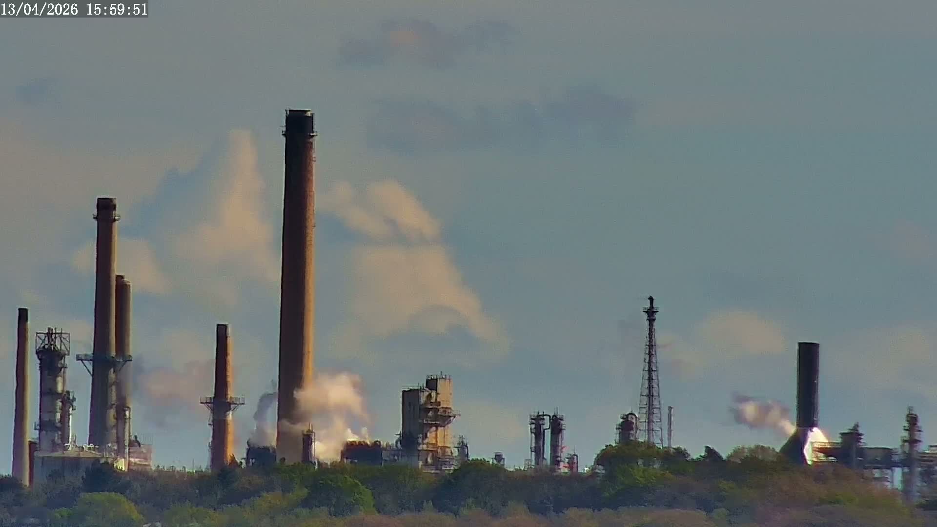 A clear dawn or dusk sky hangs over an industrial scene featuring the top of a blue boat, a flare stack with a bright flame, extensive scaffolding, and numerous factory chimneys emitting plumes of steam.