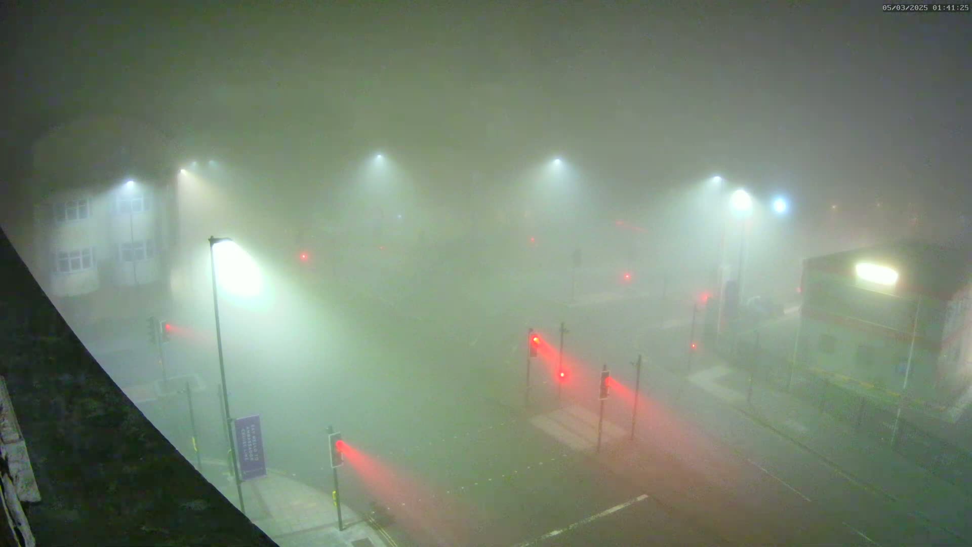 A foggy night scene shows a street intersection with several streetlights illuminating the dense fog and red traffic signals.