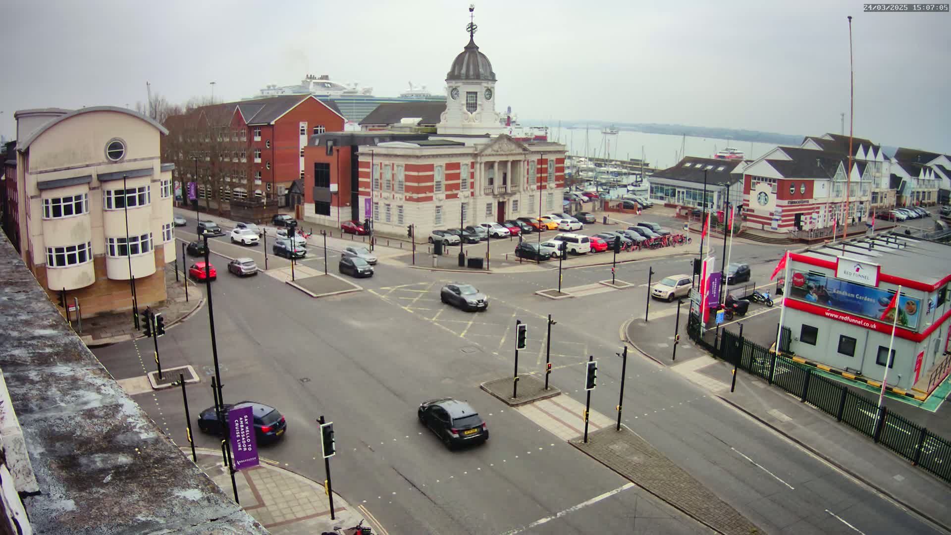 A street intersection with several cars, surrounded by buildings including a large brick building with a dome, under an overcast sky.