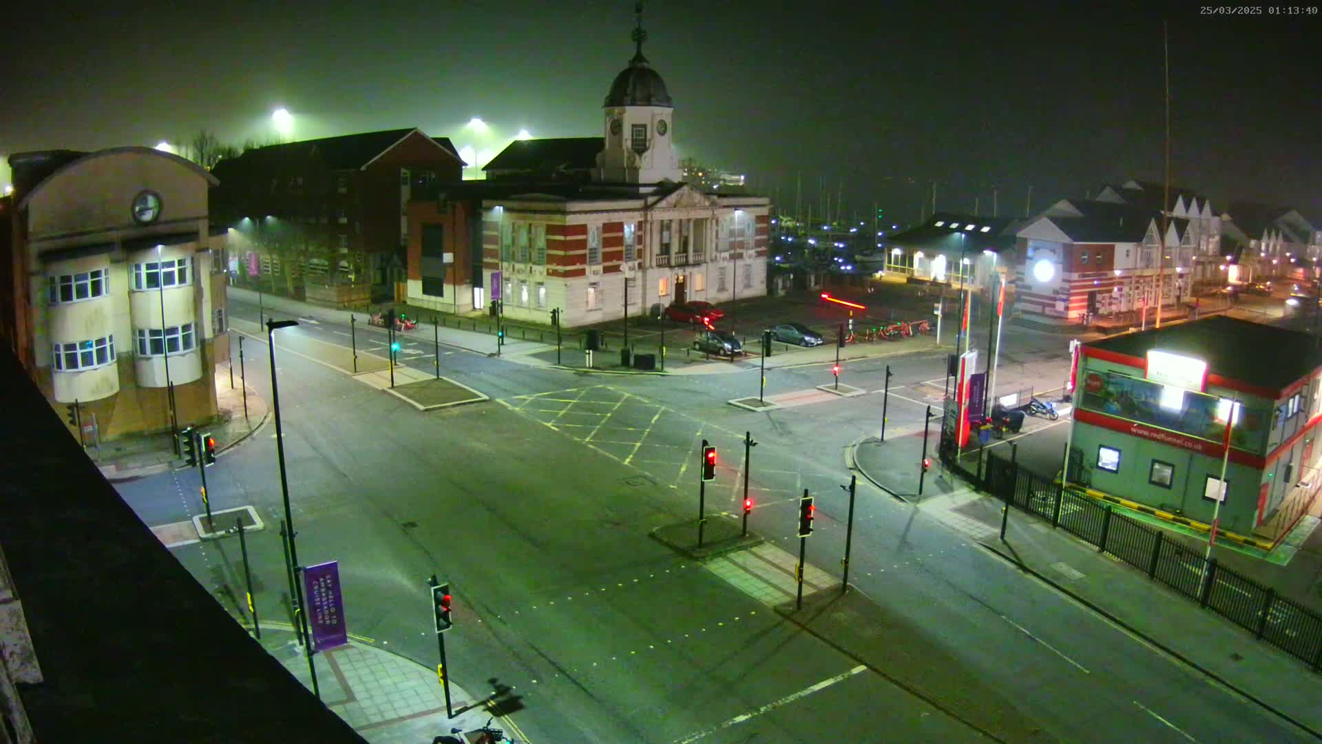 A foggy night scene shows a multi-lane intersection with traffic lights, several buildings including a large brick structure with a dome, and a few parked cars.