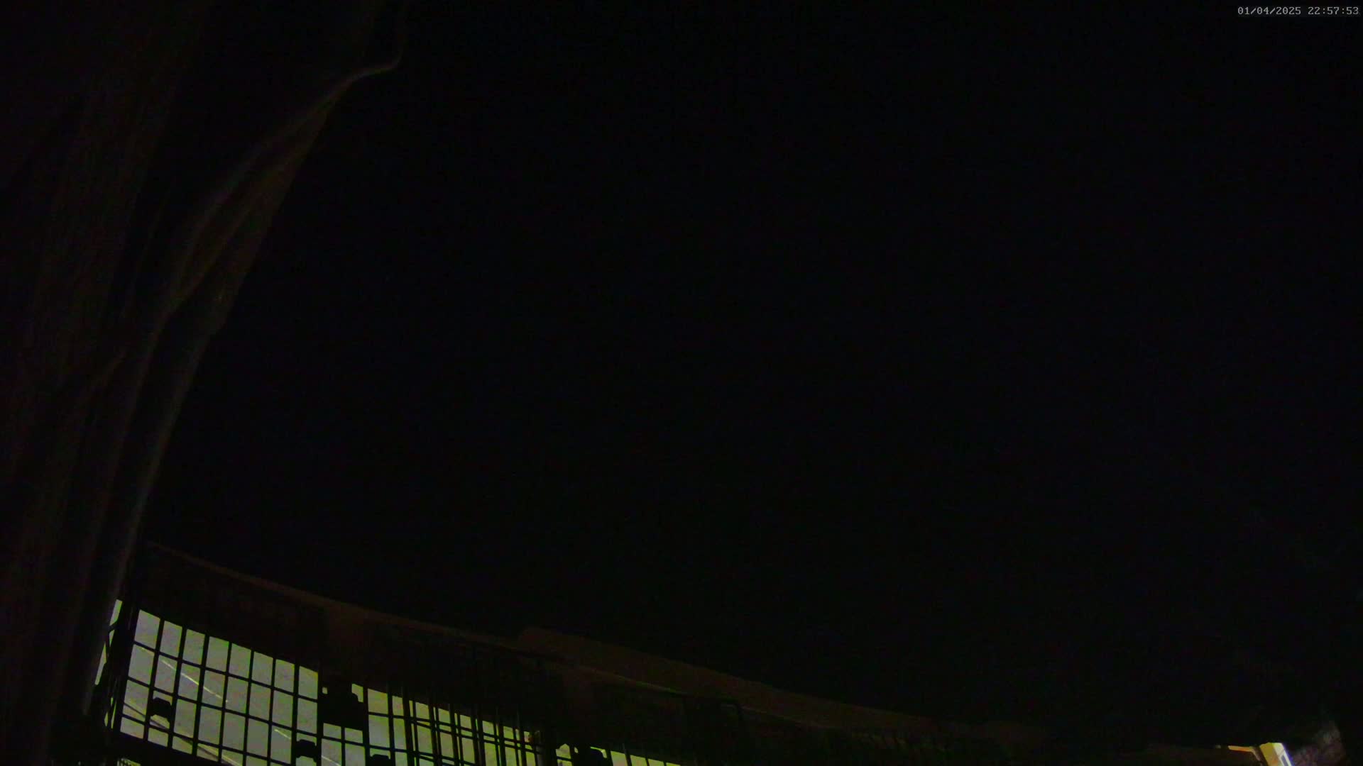 A low-angle nighttime view shows a dark, clear sky above a portion of a structure with a grid-like pattern.