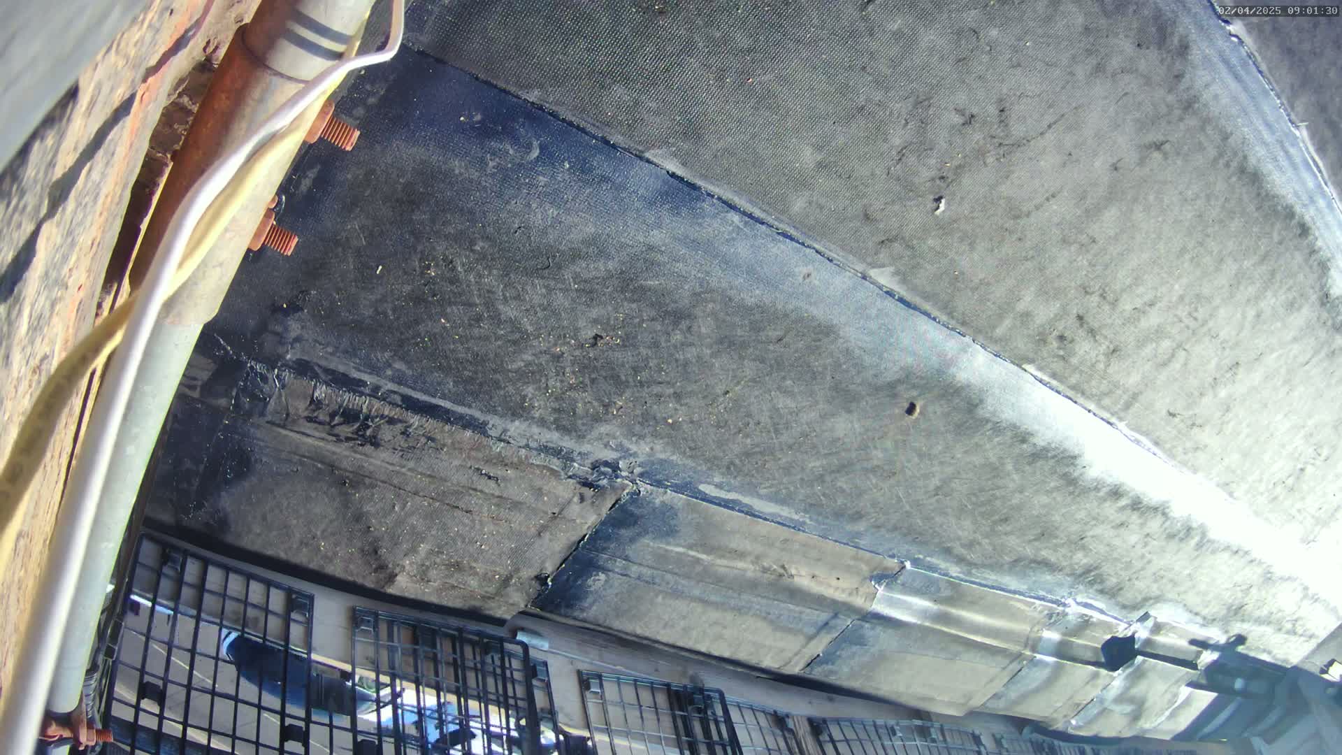 A view from underneath a vehicle shows a dirty, patched undercarriage with a section of metal grating visible below.