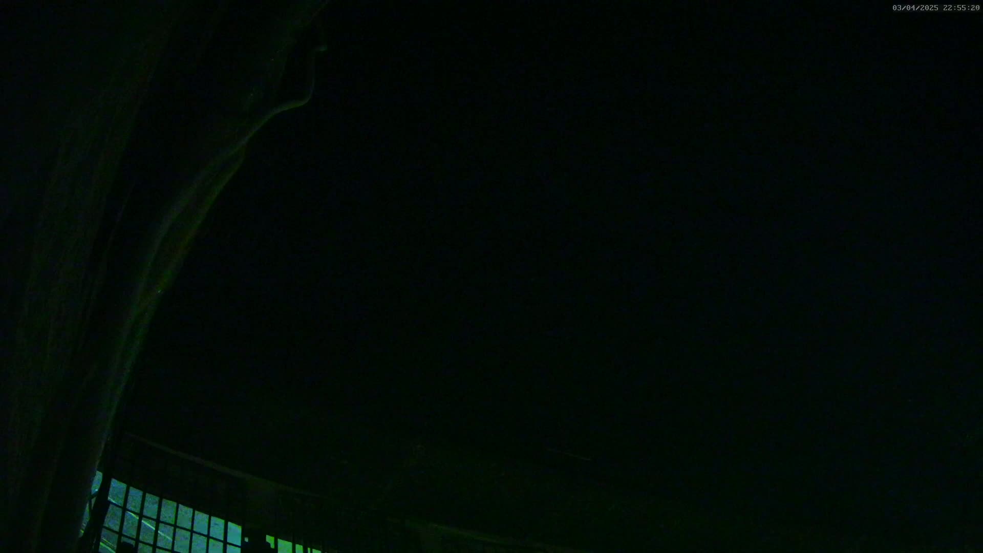 A nighttime, low-angle view shows a dark sky above a portion of a structure with a section of a window visible at the bottom.