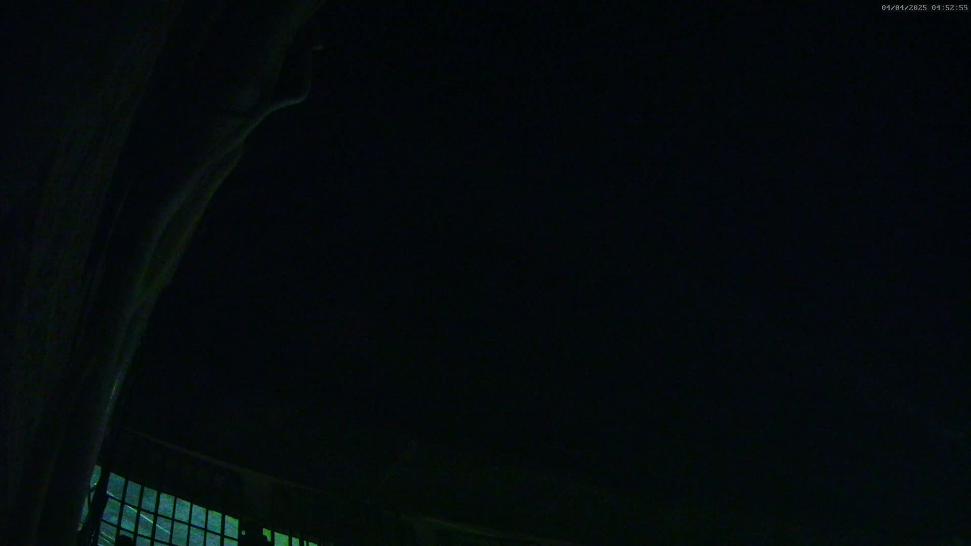 A dark, nighttime scene shows a portion of a building's exterior with a window, viewed from a low angle.