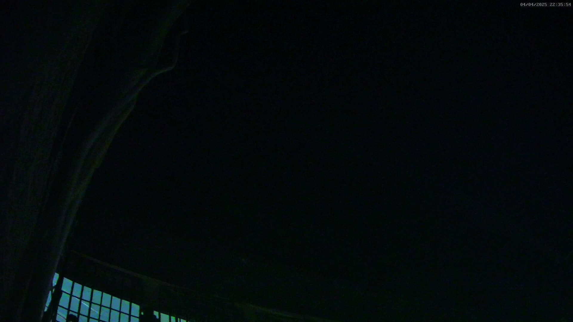 A low-angle, nighttime view shows a dark, mostly obscured structure with a grid of faintly lit windows at the bottom, against a pitch-black sky.