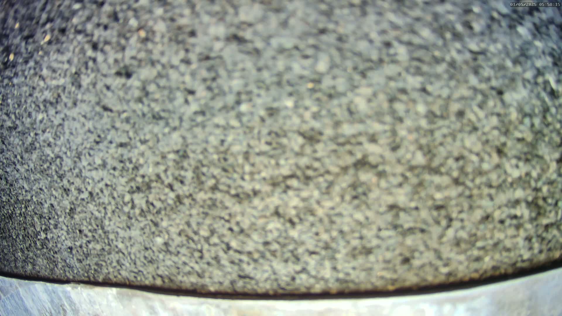A close-up shows a dark gray, rough-textured surface, possibly stone or asphalt, with a thin metallic band at the bottom.