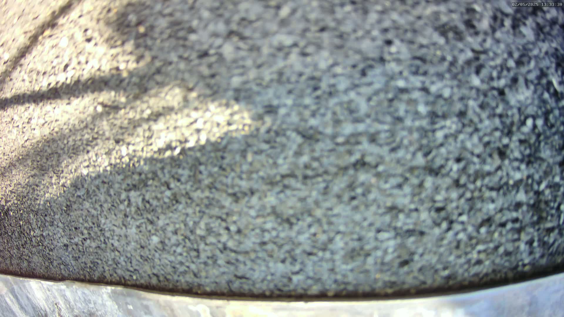 A close-up view shows a dark gray, textured surface, possibly asphalt, with a shadow cast across it in sunny conditions.