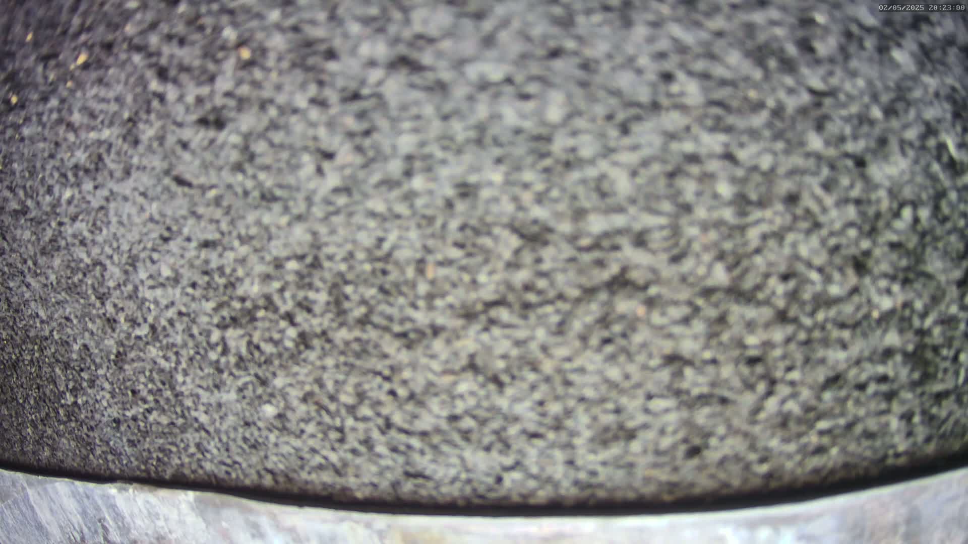 A close-up shows a dark gray, rough-textured surface, possibly asphalt or stone, with a lighter gray band at the bottom.