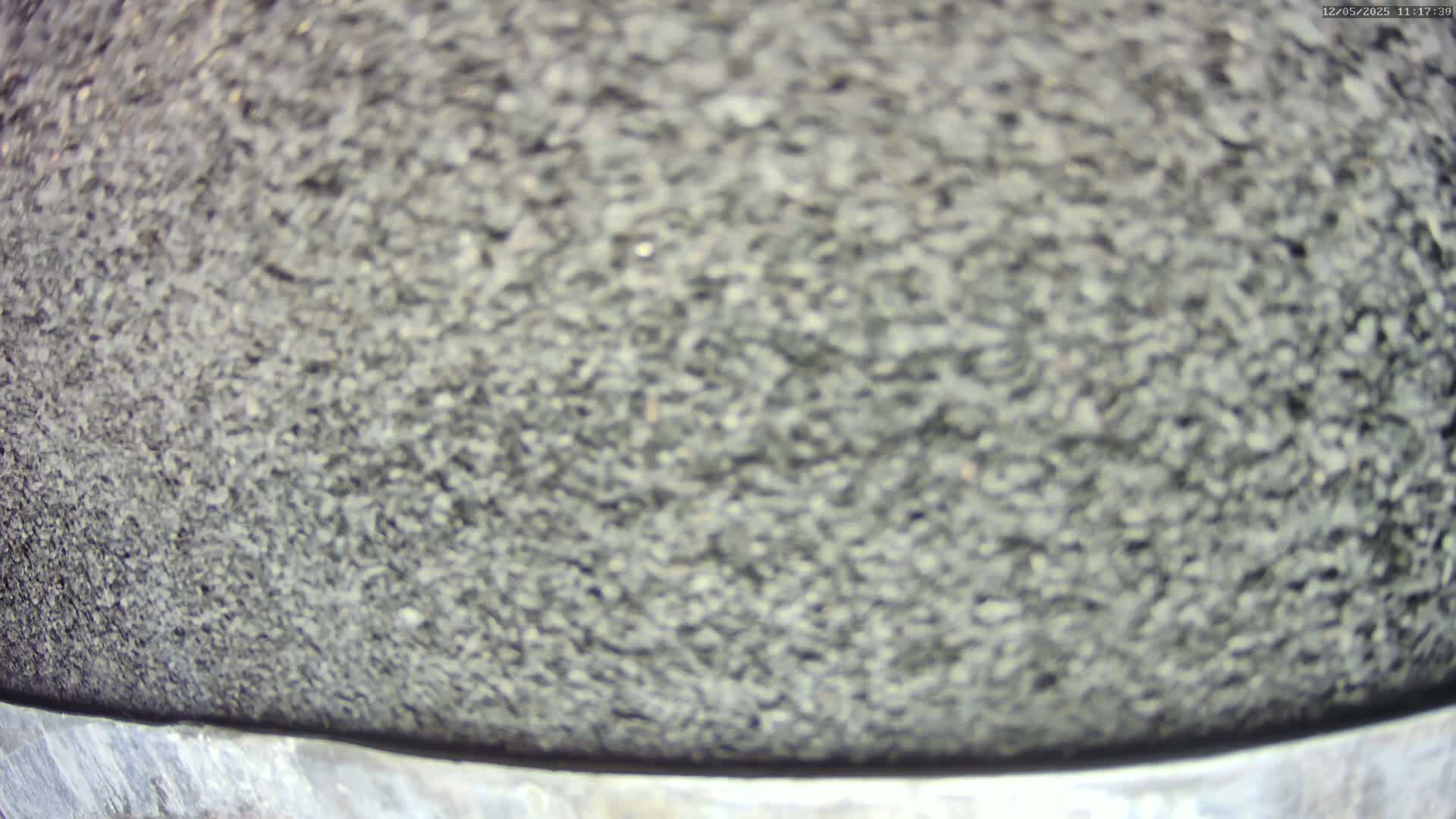 A blurry close-up shows a dark gray, coarse, textured surface, possibly asphalt, with a lighter gray metal edge at the bottom.