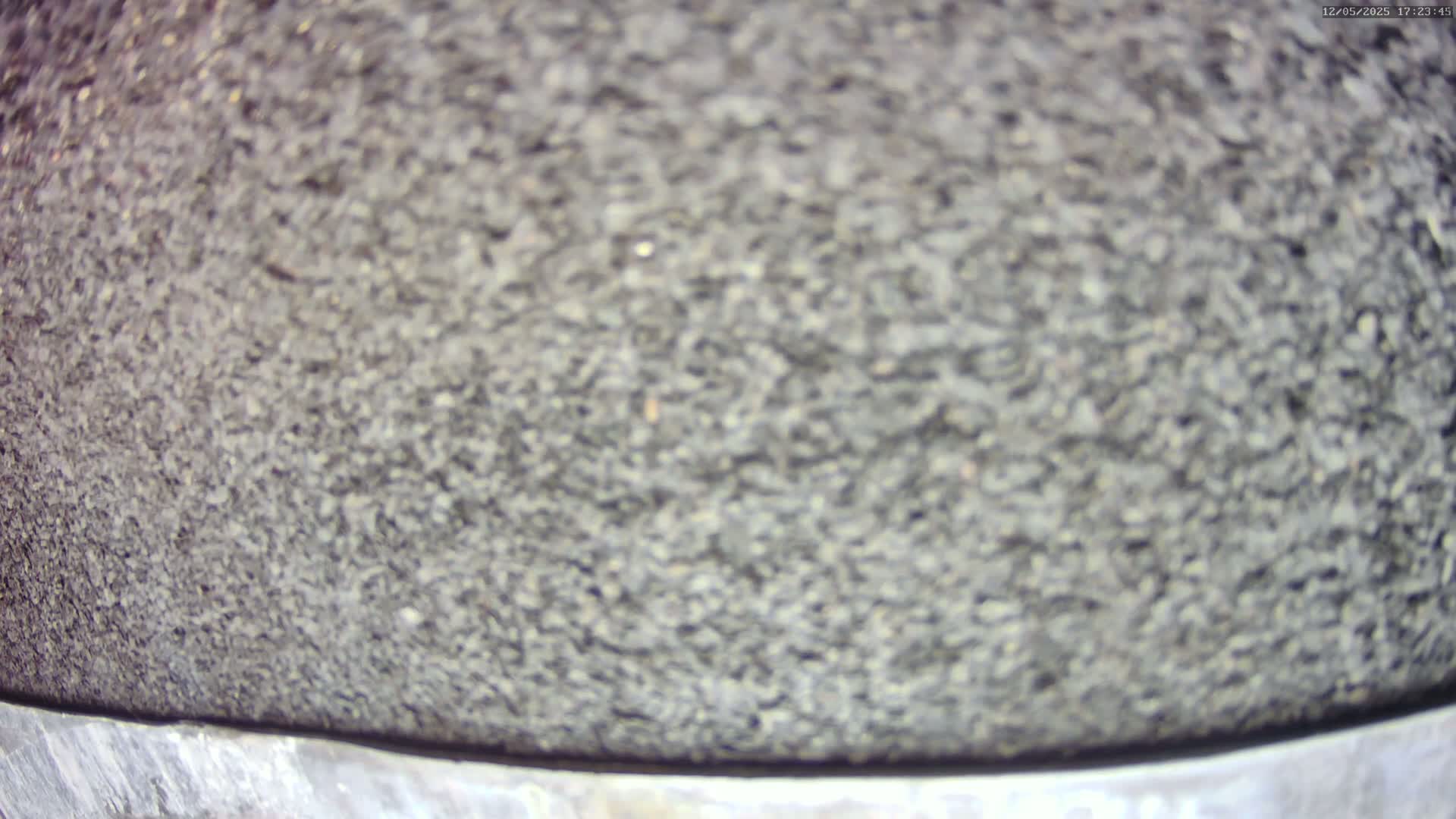 A close-up shows a dark gray, granular surface with a slightly blurry texture, atop a lighter gray, metallic band.
