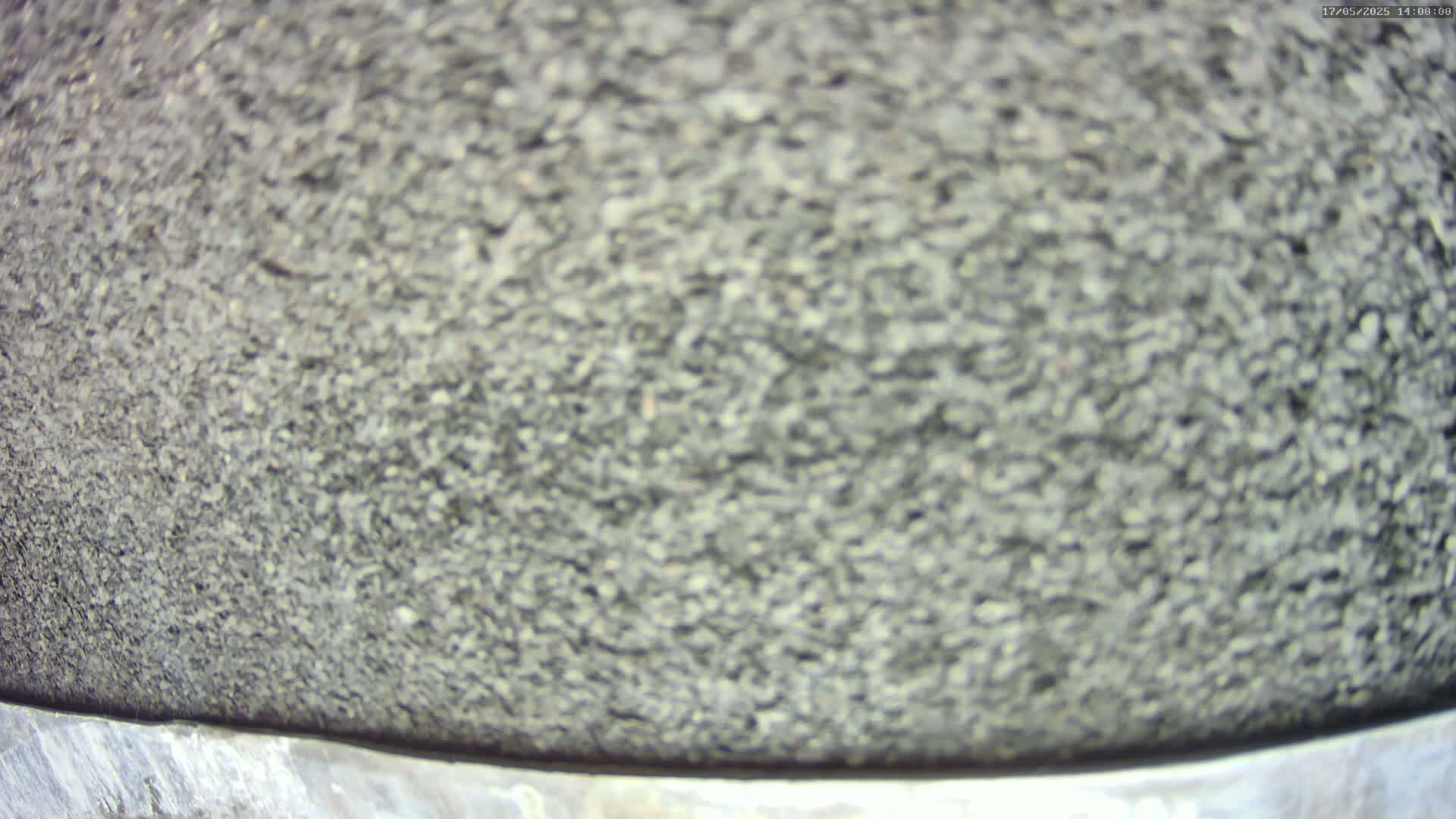 A close-up view shows a blurry, textured surface that resembles asphalt or a similar coarse material.