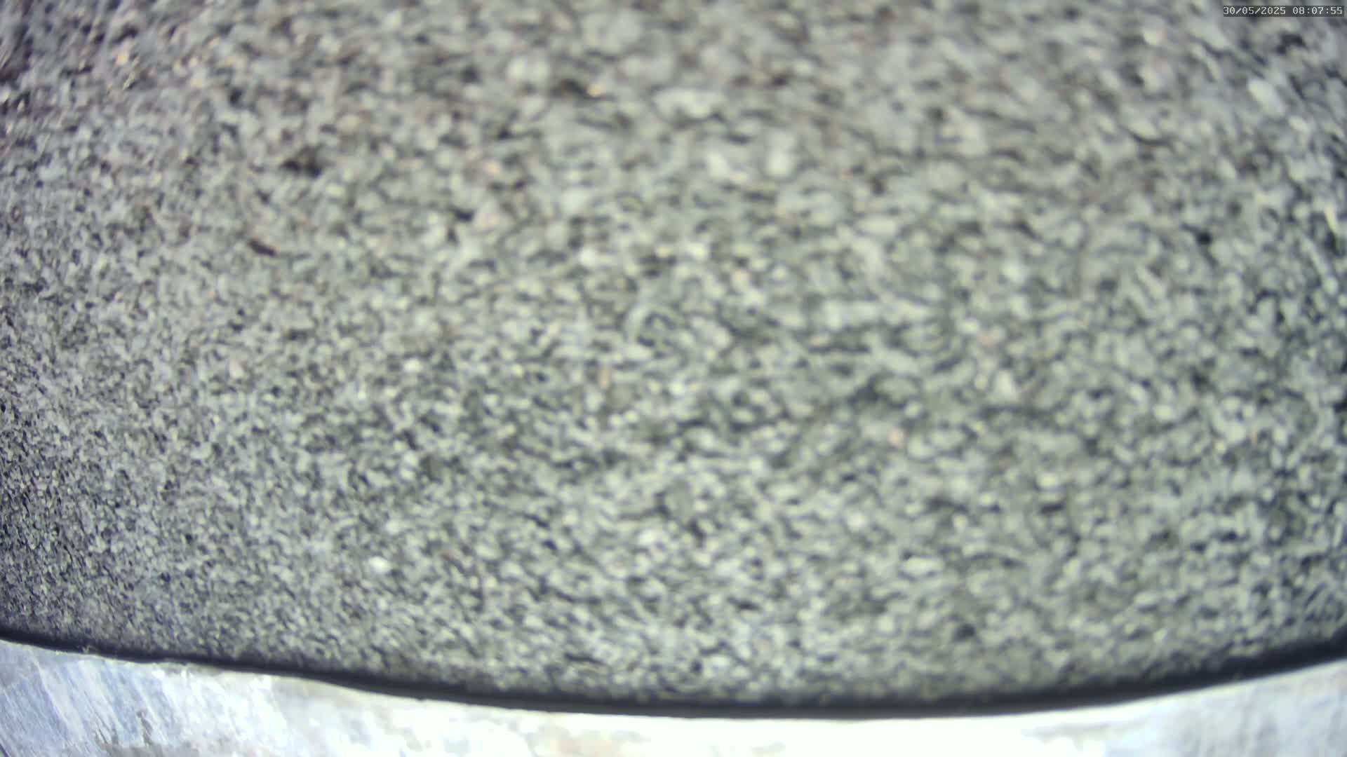 A close-up view shows a blurry, dark gray granular surface, possibly asphalt or gravel, atop a metallic band.