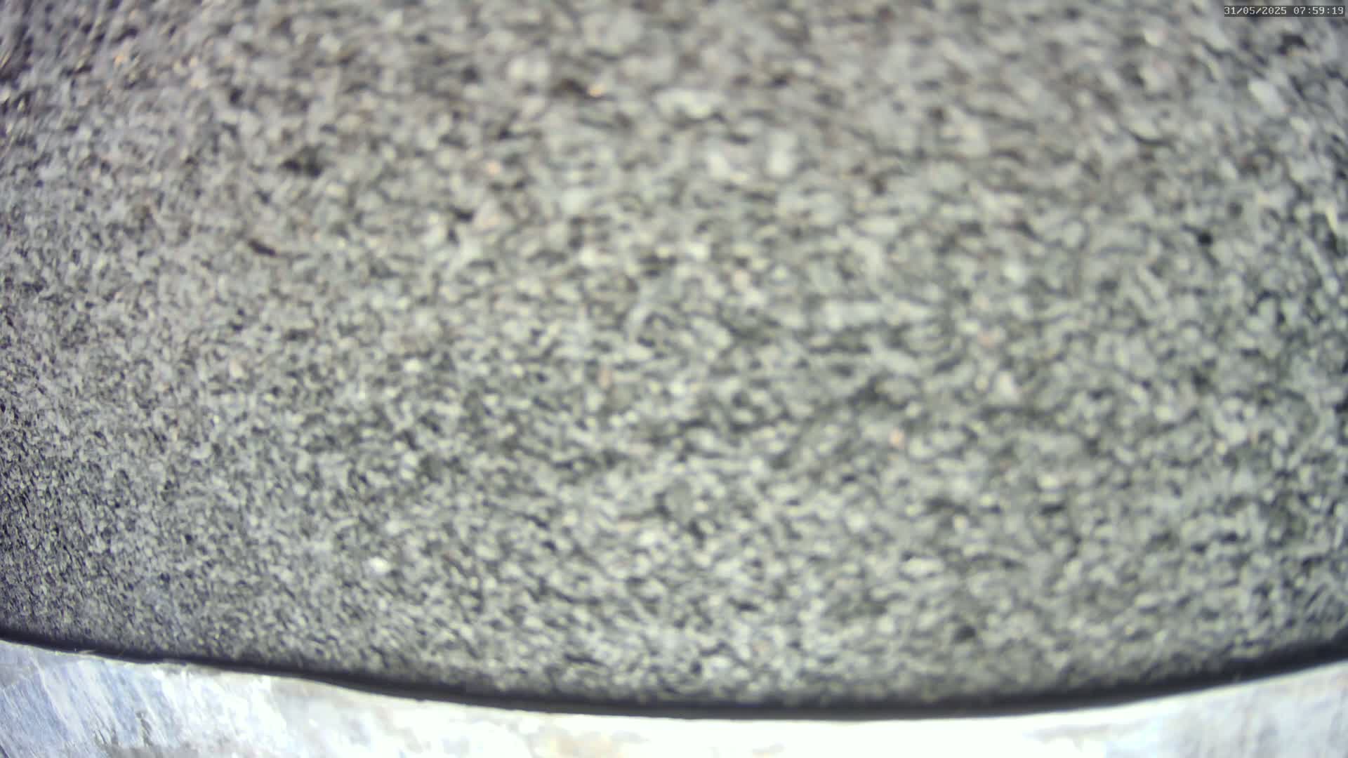 A close-up view shows a dark gray, granular surface that appears to be a coarse material, possibly asphalt or gravel.
