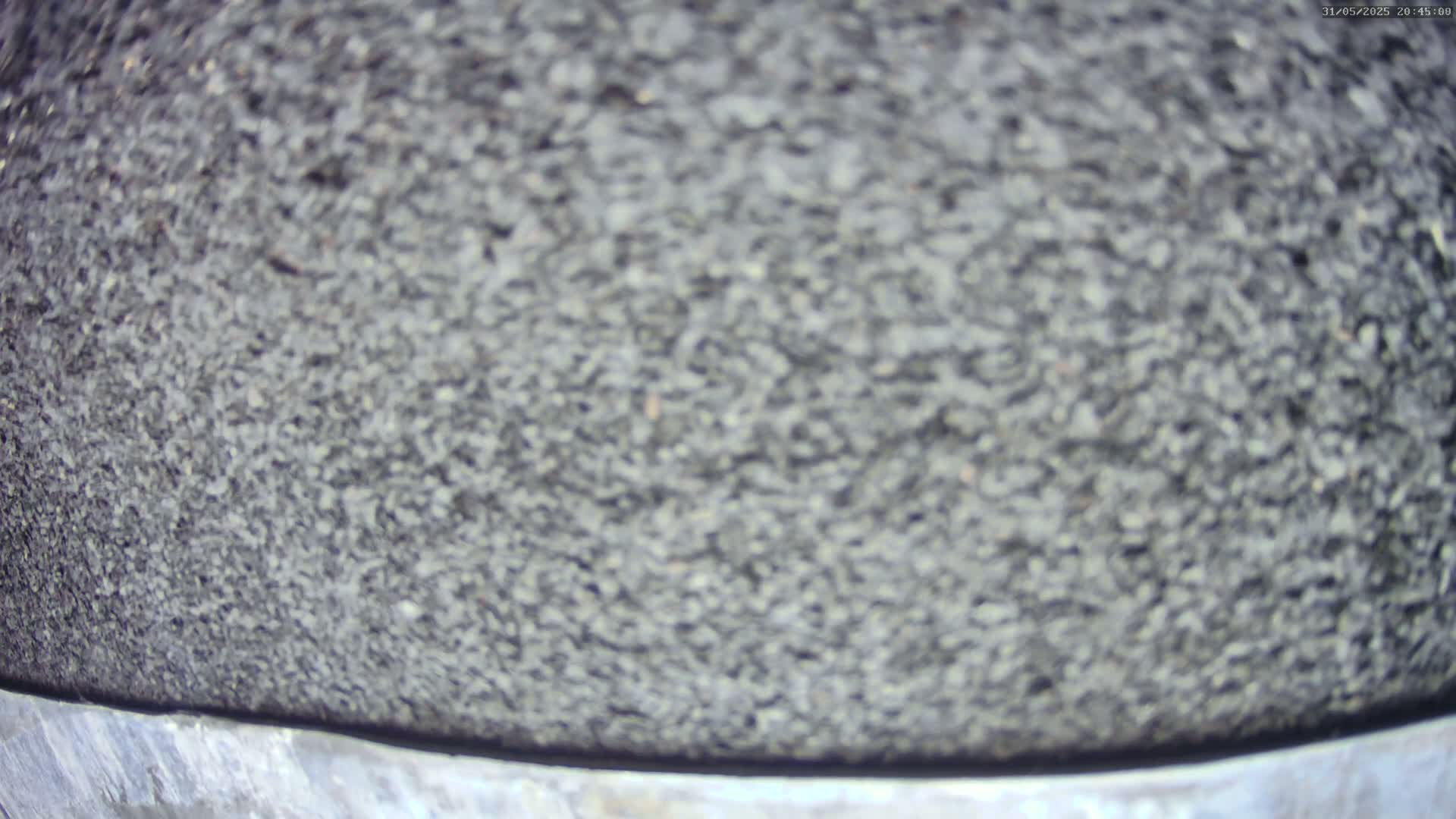 A close-up view shows a dark gray, granular surface, possibly asphalt or similar material, with a metallic edge visible at the bottom.