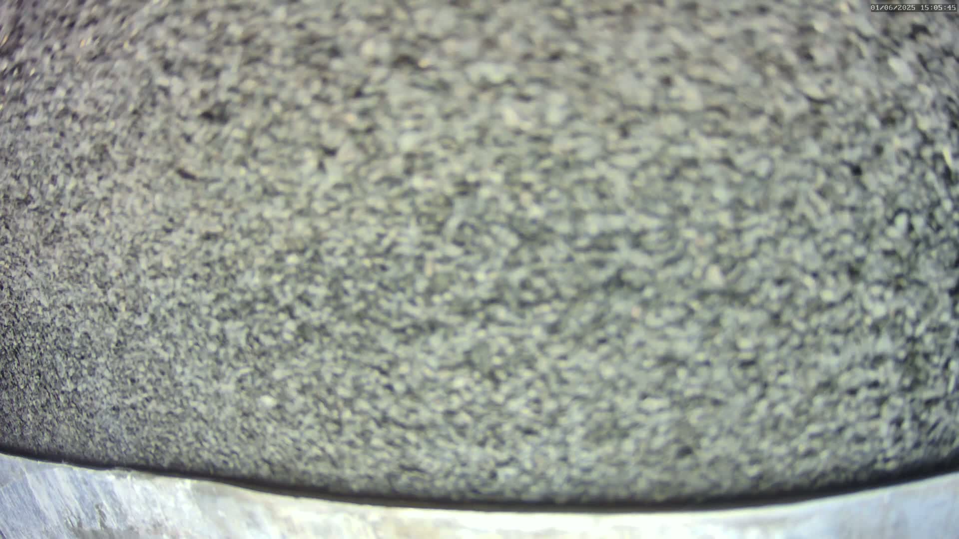 A close-up view shows a large quantity of dark gray, small stones or gravel, partially contained by a metallic edge.