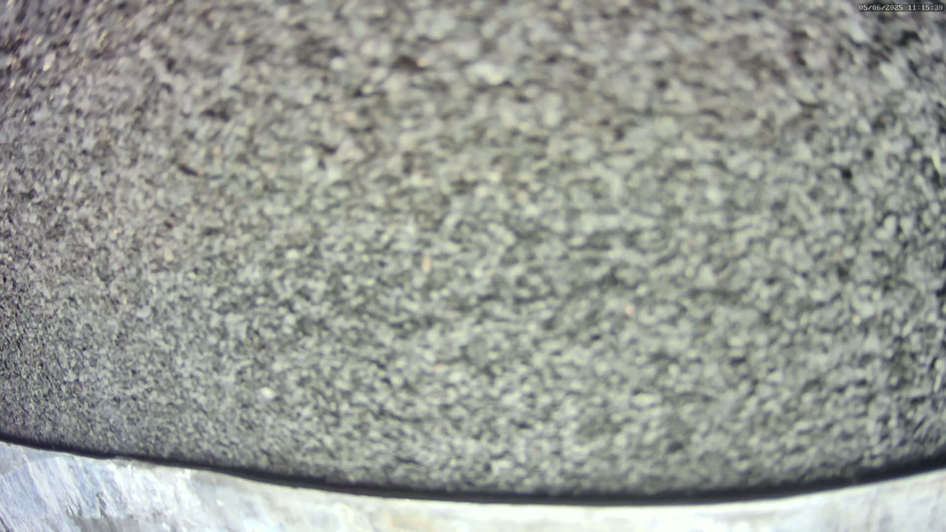 A blurry close-up of a dark gray, granular surface, possibly asphalt or similar material.