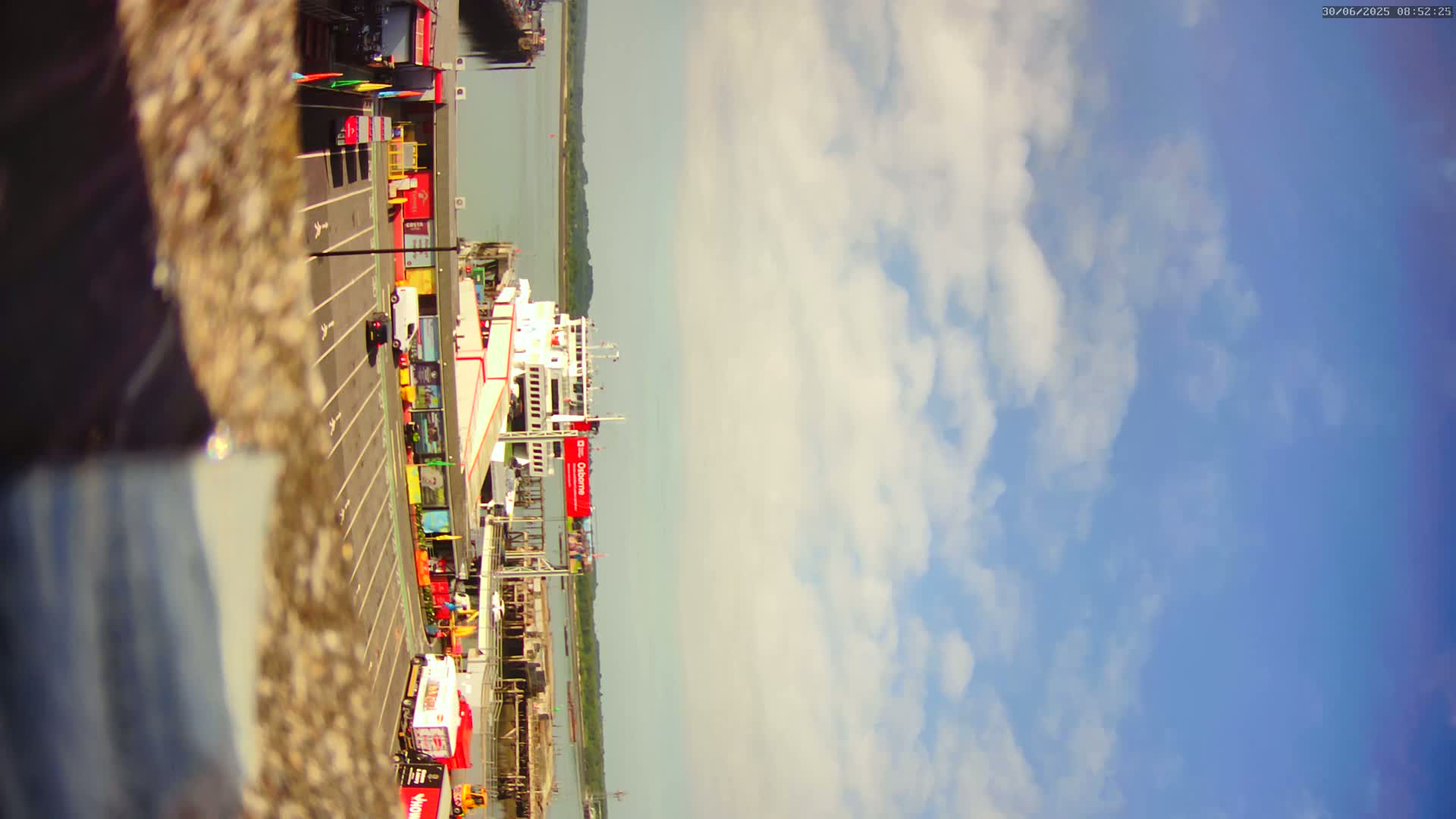 A ferry is docked at a terminal under a partly cloudy sky.