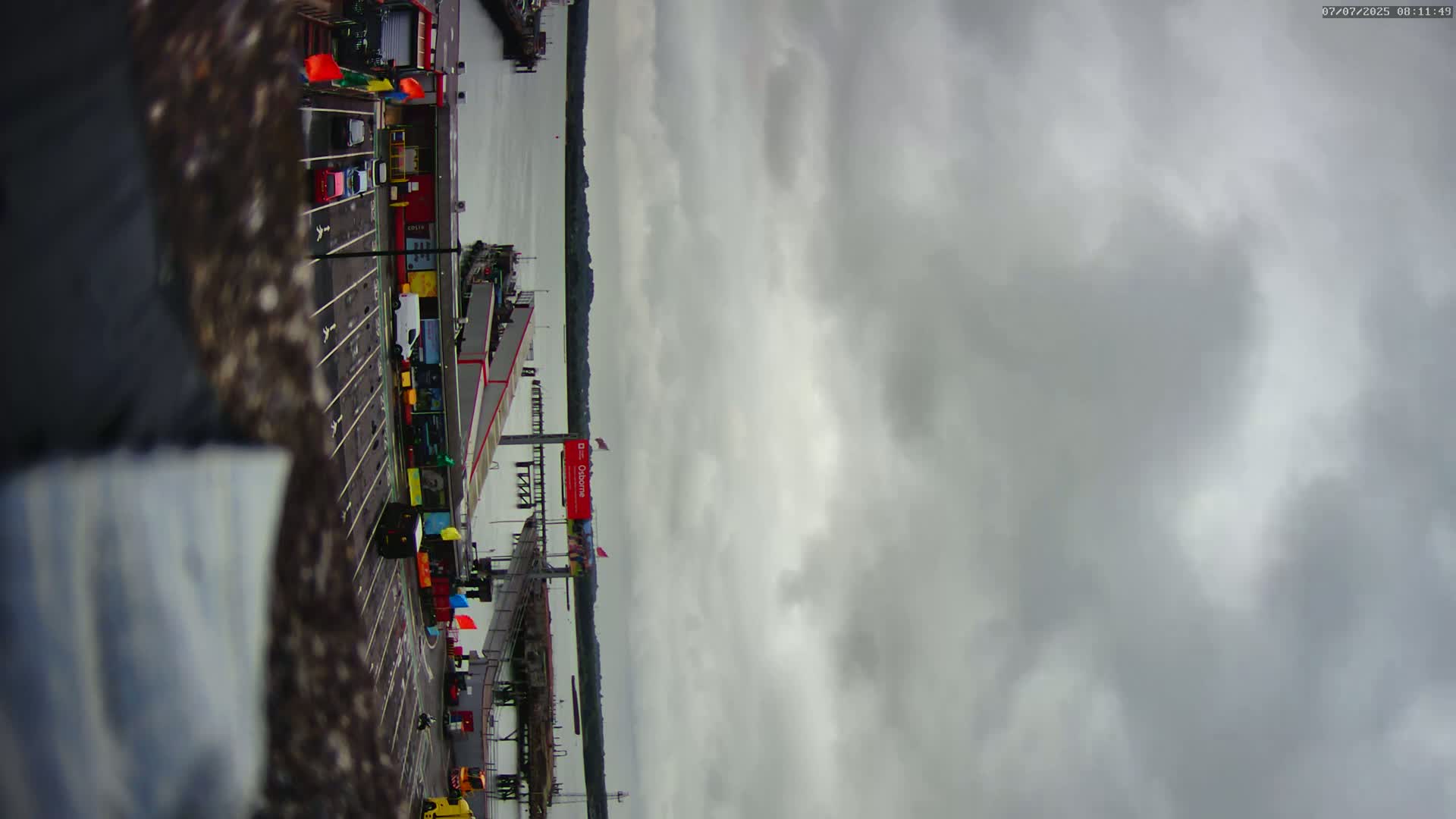 A ferry terminal with several vehicles parked, under an overcast sky.