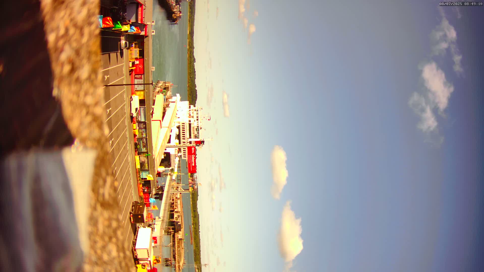 A ferry is docked at a port under a mostly clear sky with a few fluffy clouds.