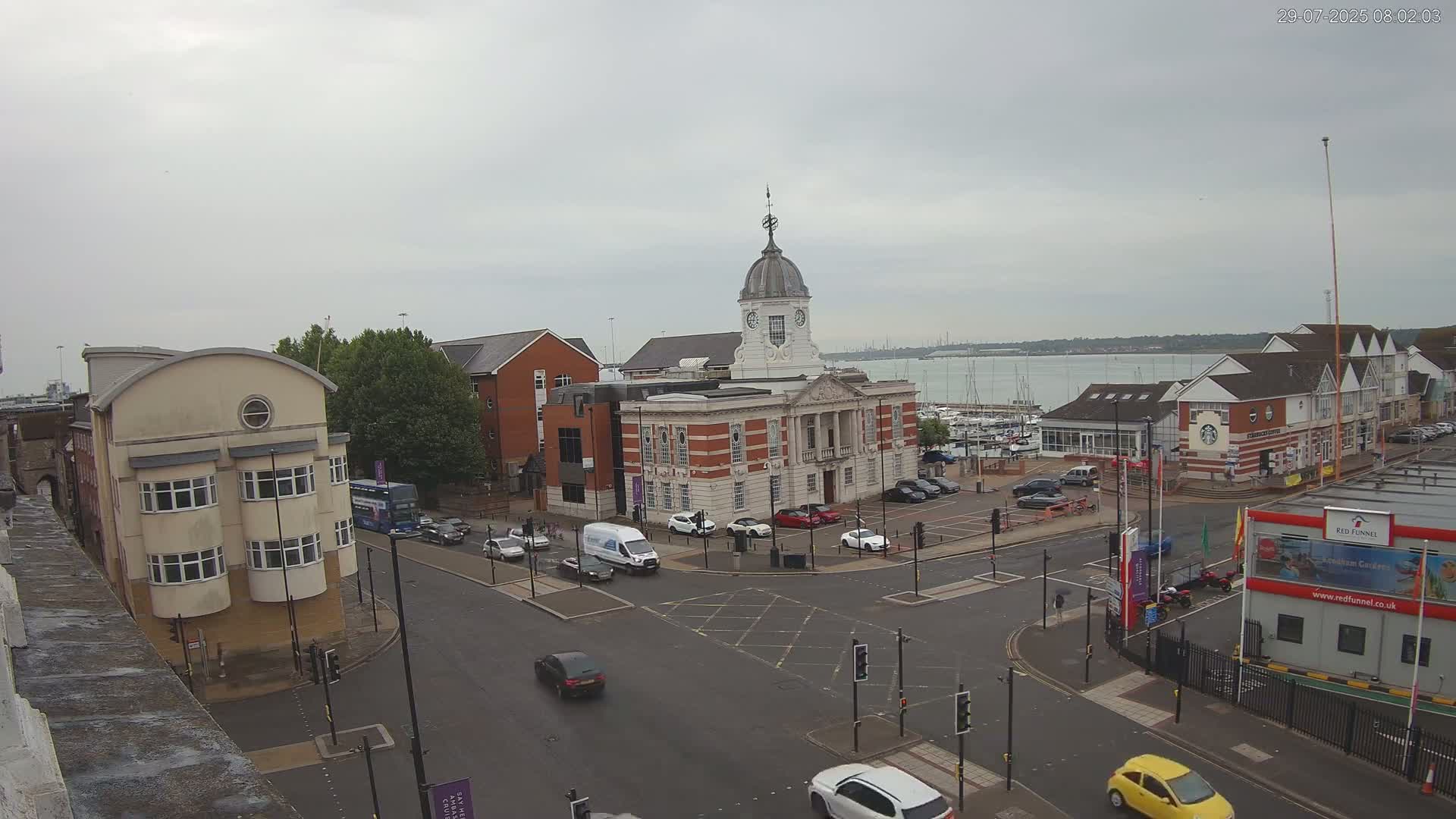 An overcast day reveals a city street scene with several buildings, including a large brick building with a dome, and a marina visible in the distance.