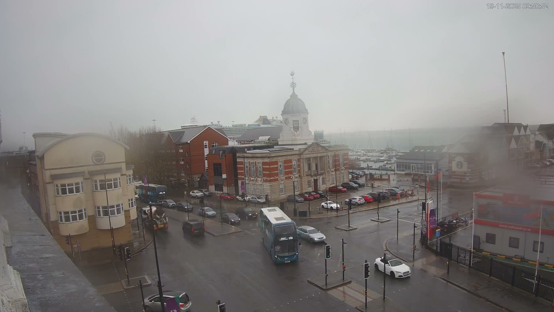 A foggy and wet urban scene reveals a classic domed building, busy streets with vehicles, and a marina packed with boats, all under a pervasive gray sky.