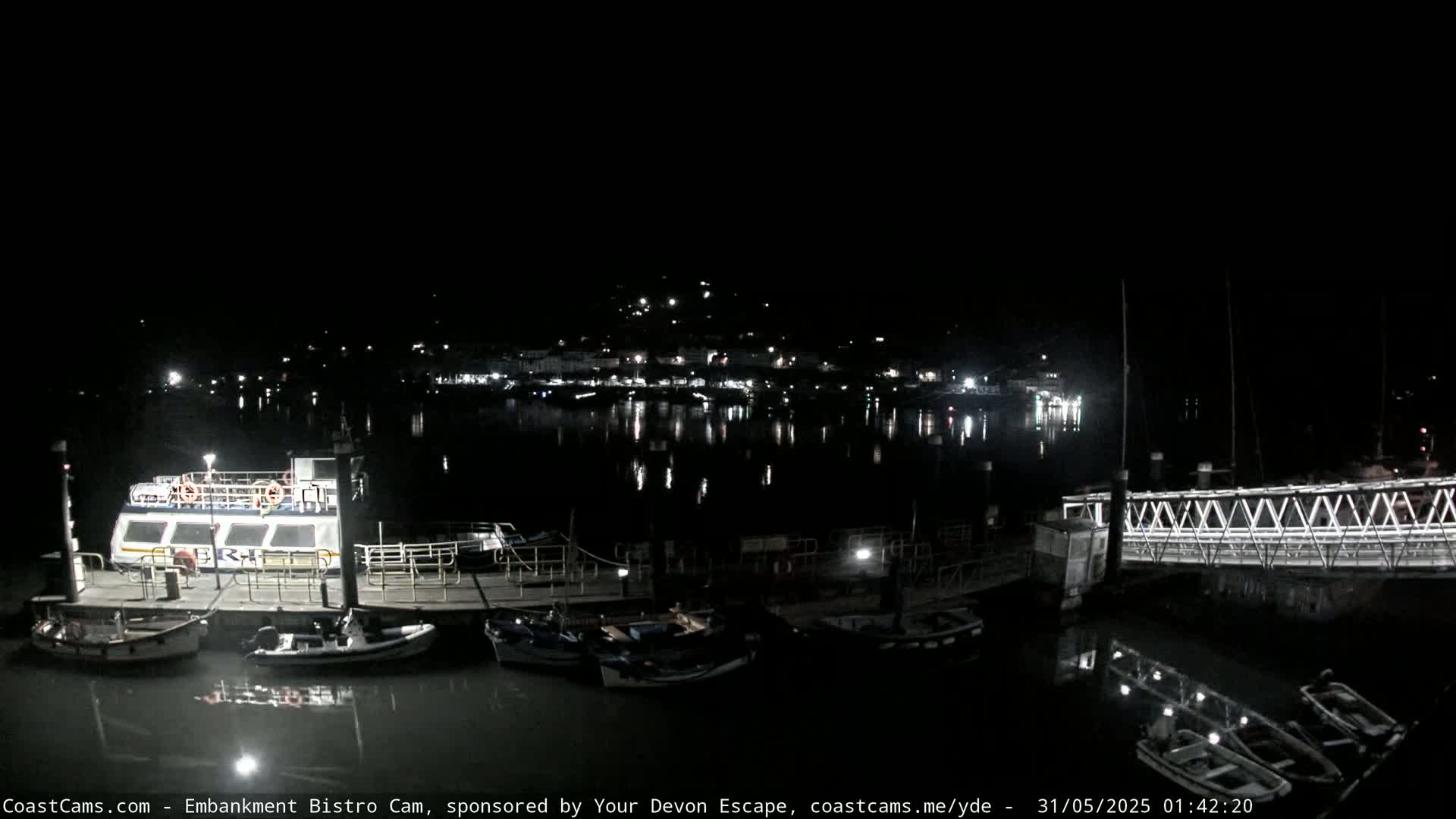 A nighttime harbor scene shows a docked ferry and several smaller boats, with a town's lights reflecting in the calm water.