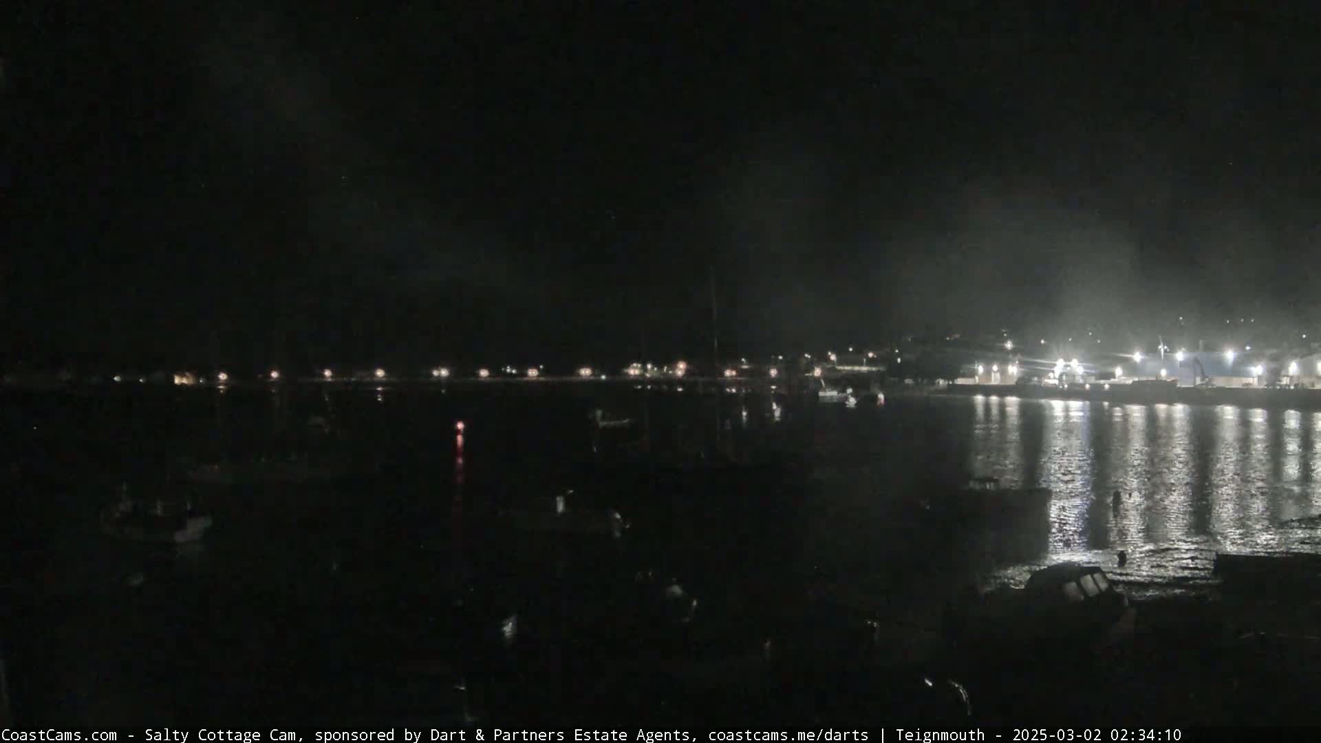 A nighttime view of a harbor with boats and lights reflecting on calm water.
