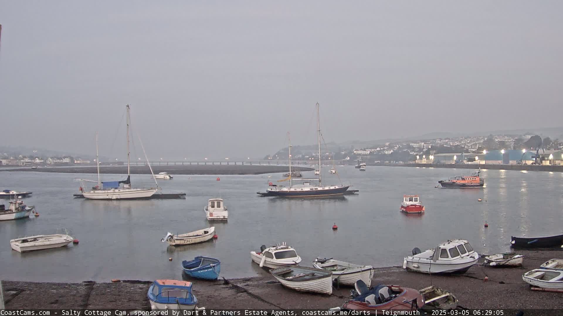 Several sailboats and motorboats are moored in a calm, overcast harbor.