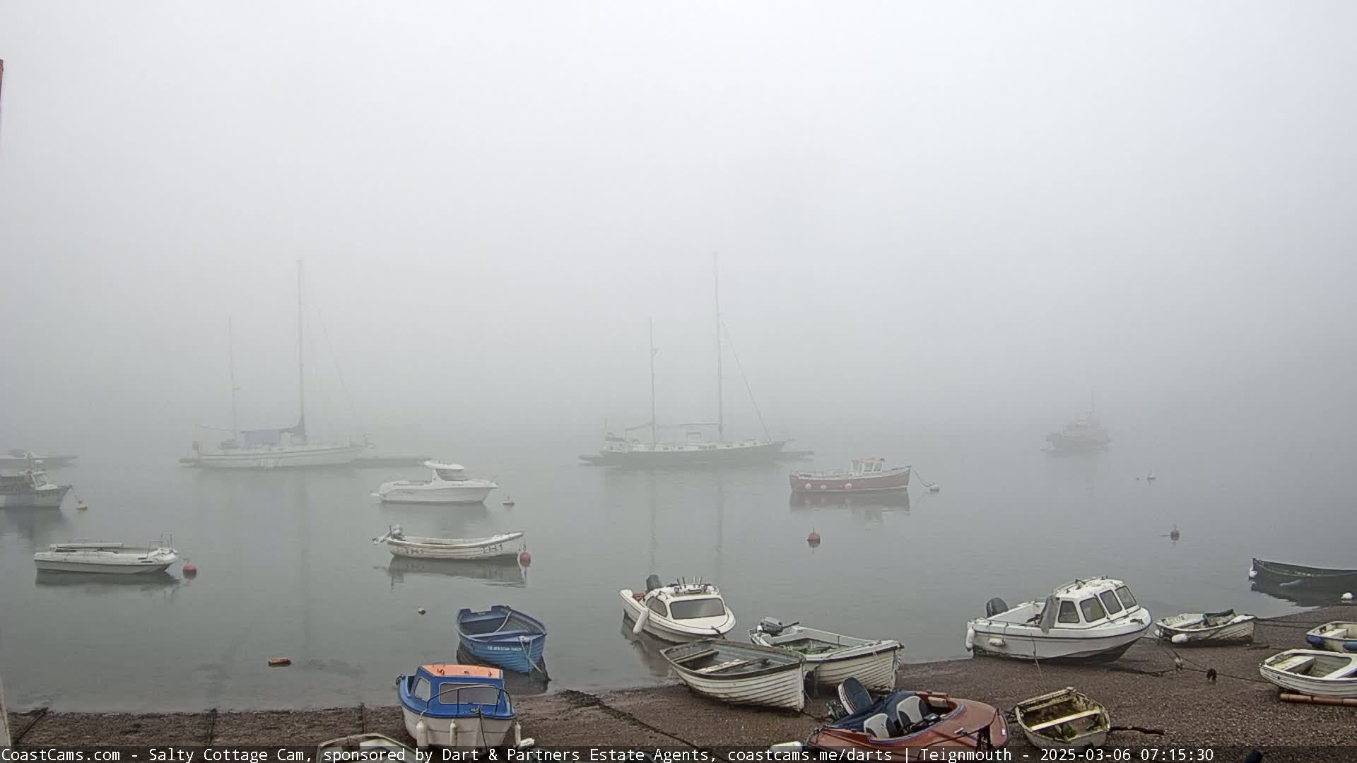 Several boats are moored in a harbor shrouded in thick fog.