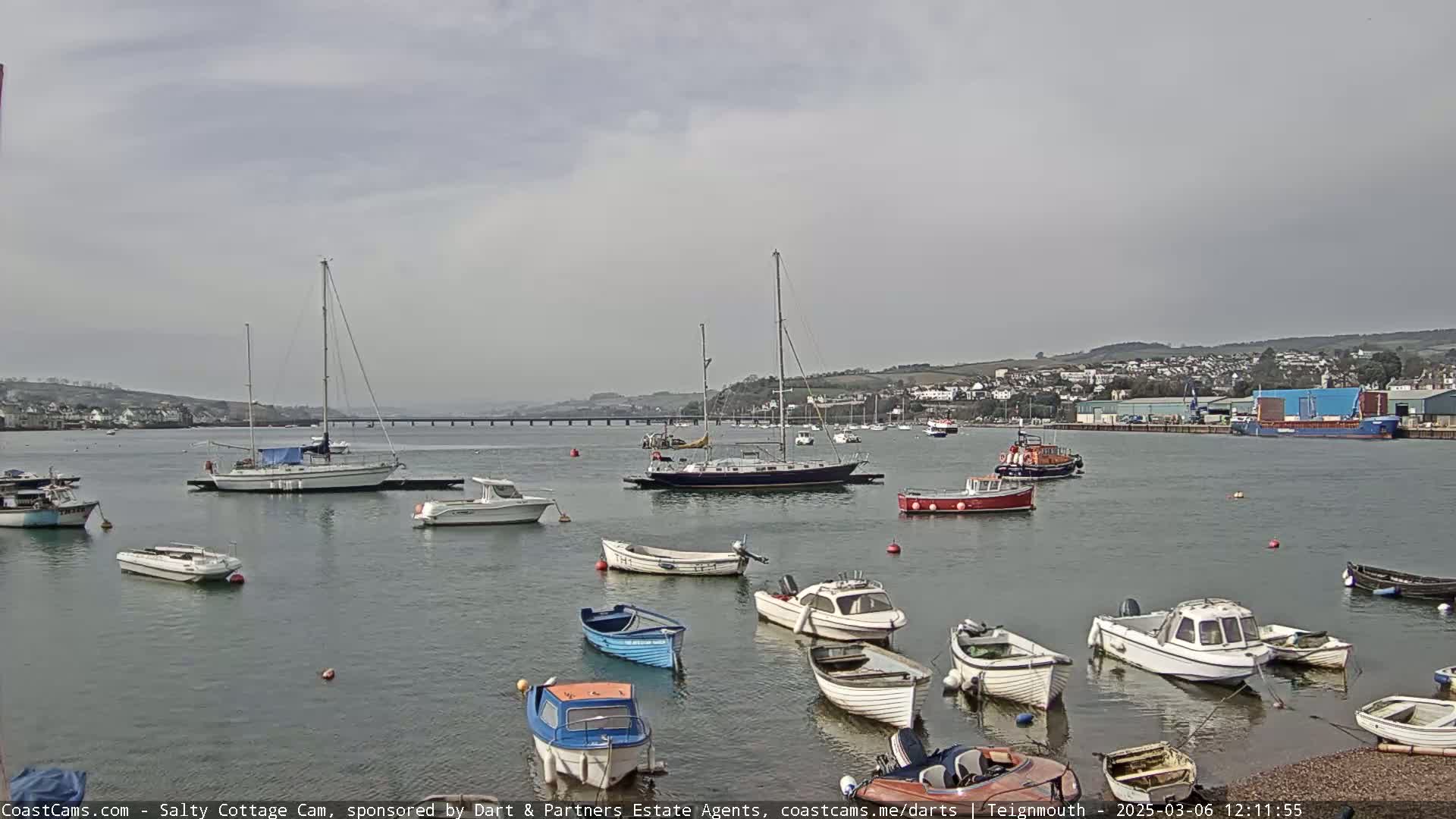 Numerous small boats and sailboats are moored in a calm harbor under an overcast sky.